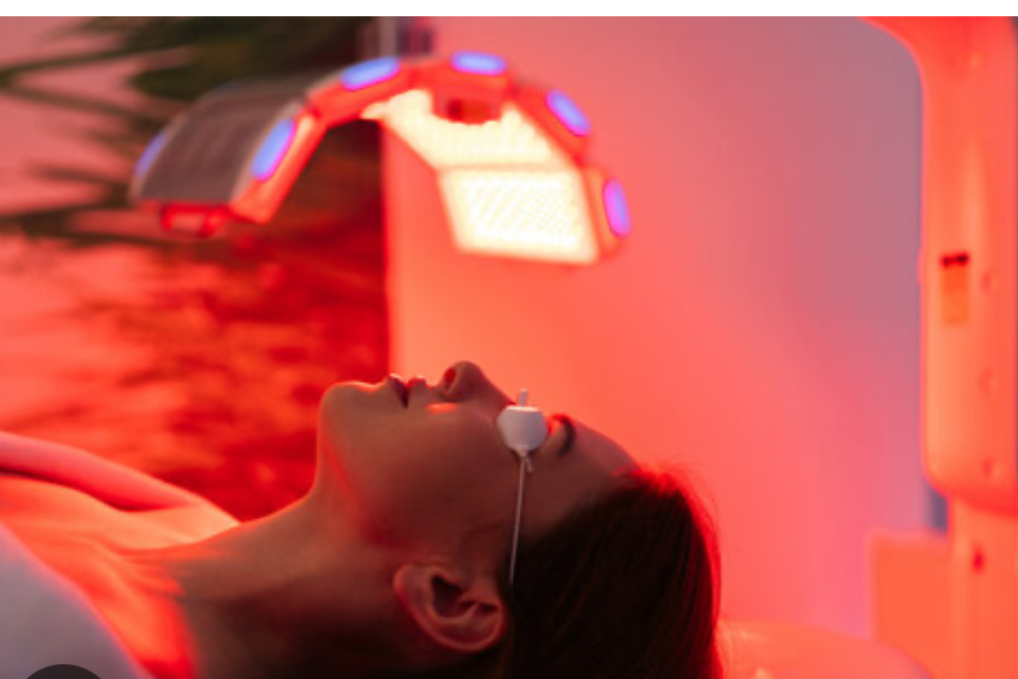 A woman lying on a bed in an MRI or a similar medical imaging machine, with a red glow from the machine's lights.