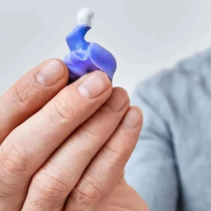 A person holding a small piece of crumpled and twisted blue and white chewing gum.