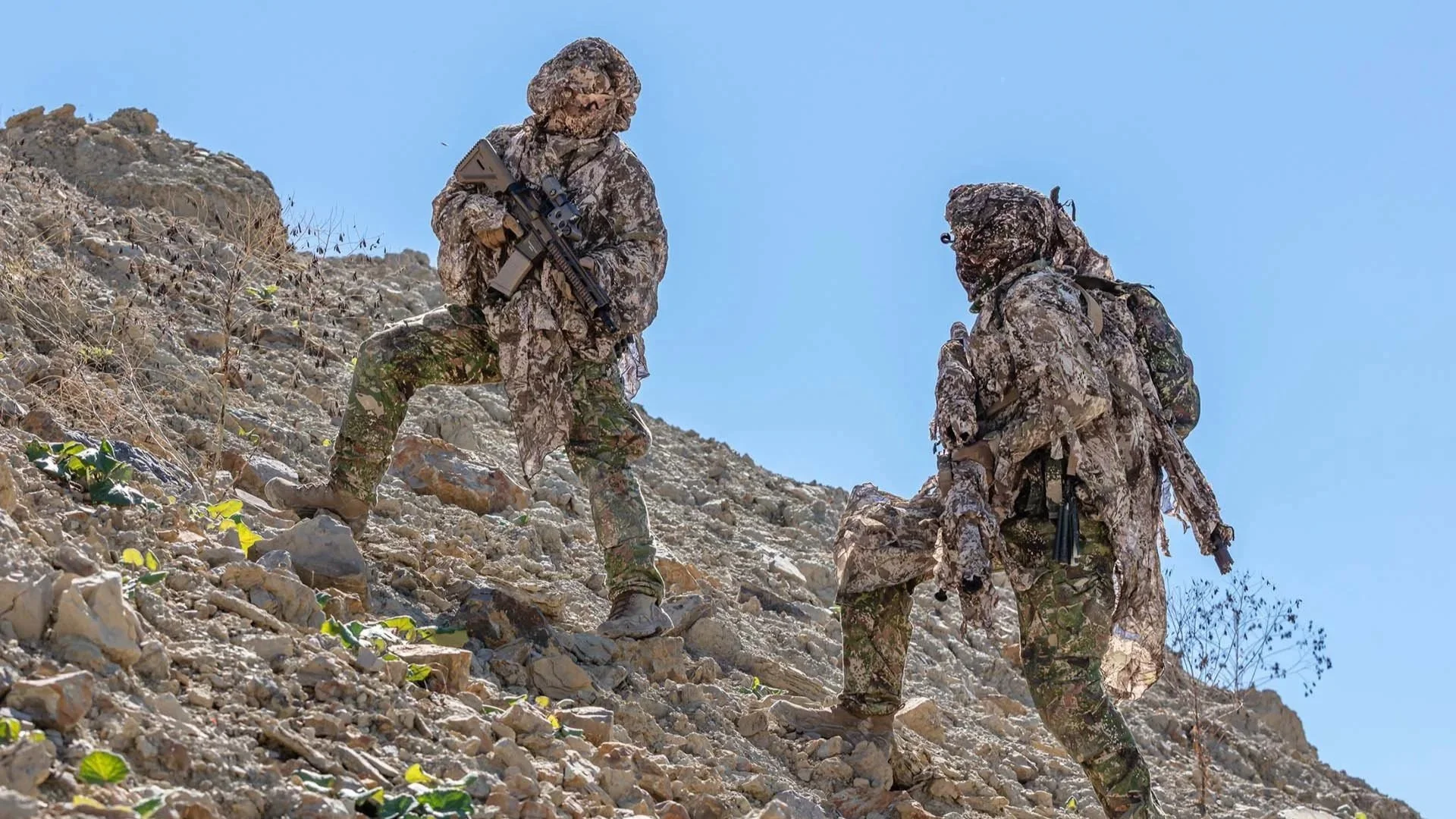 Soldaten in multispektraler Camouflage mit GHOSTHOOD Tarnsystemen beim Einsatztraining im felsigen Gelände