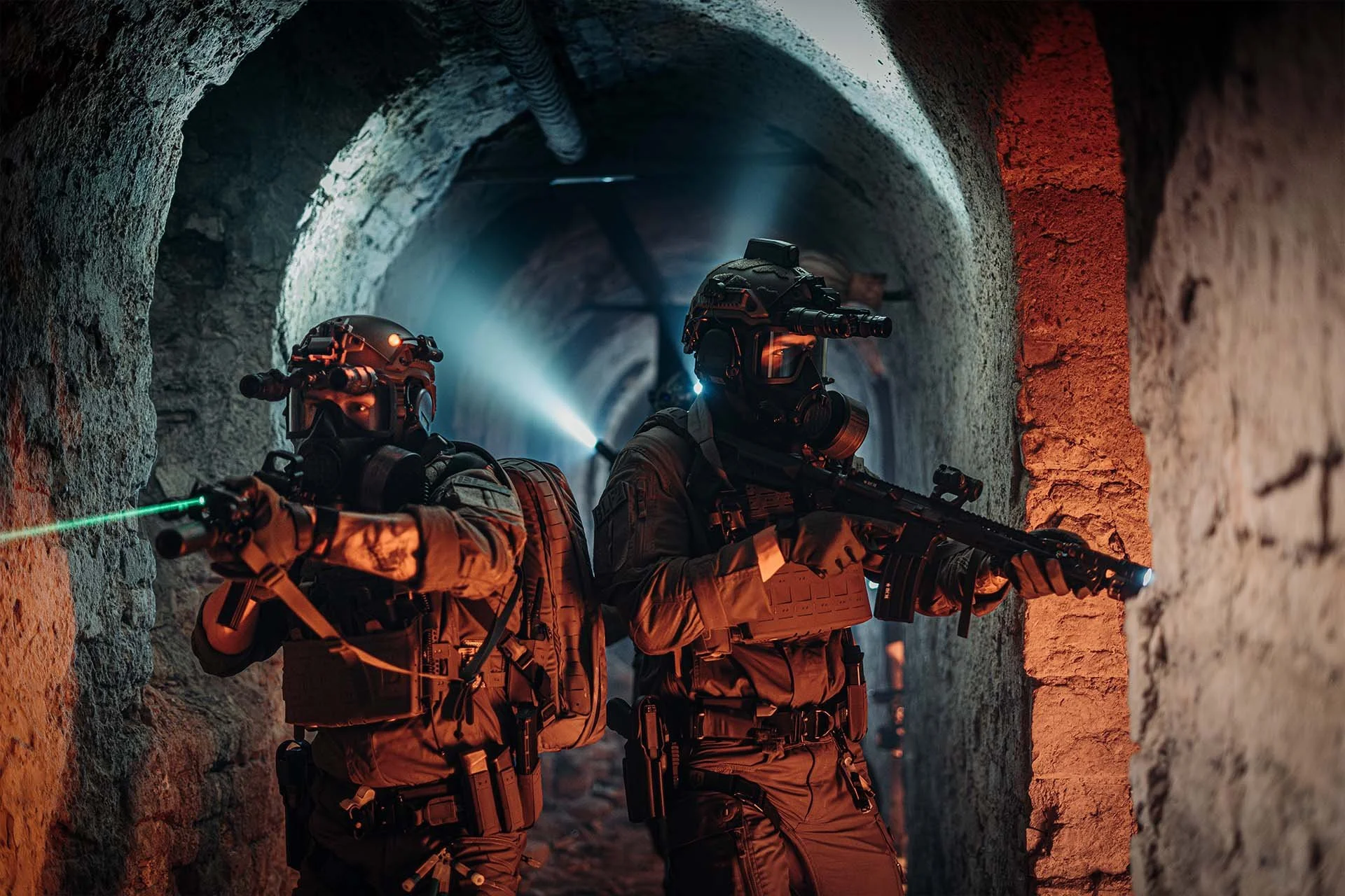 Zwei taktische Einsatzkräfte mit Nachtsichtgeräten und Waffen sichern einen engen Tunnel – ausgerüstet für Low-Light-Operationen im urbanen Umfeld.