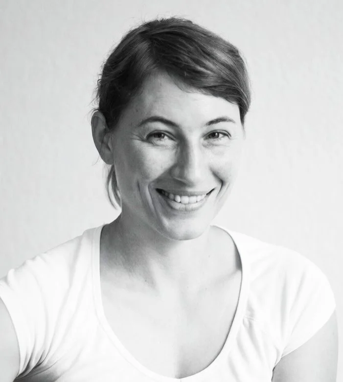 Schwarz-weiß Portrait einer lächelnden Frau mit kurzen Haaren, weißem T-Shirt, vor hellem Hintergrund.