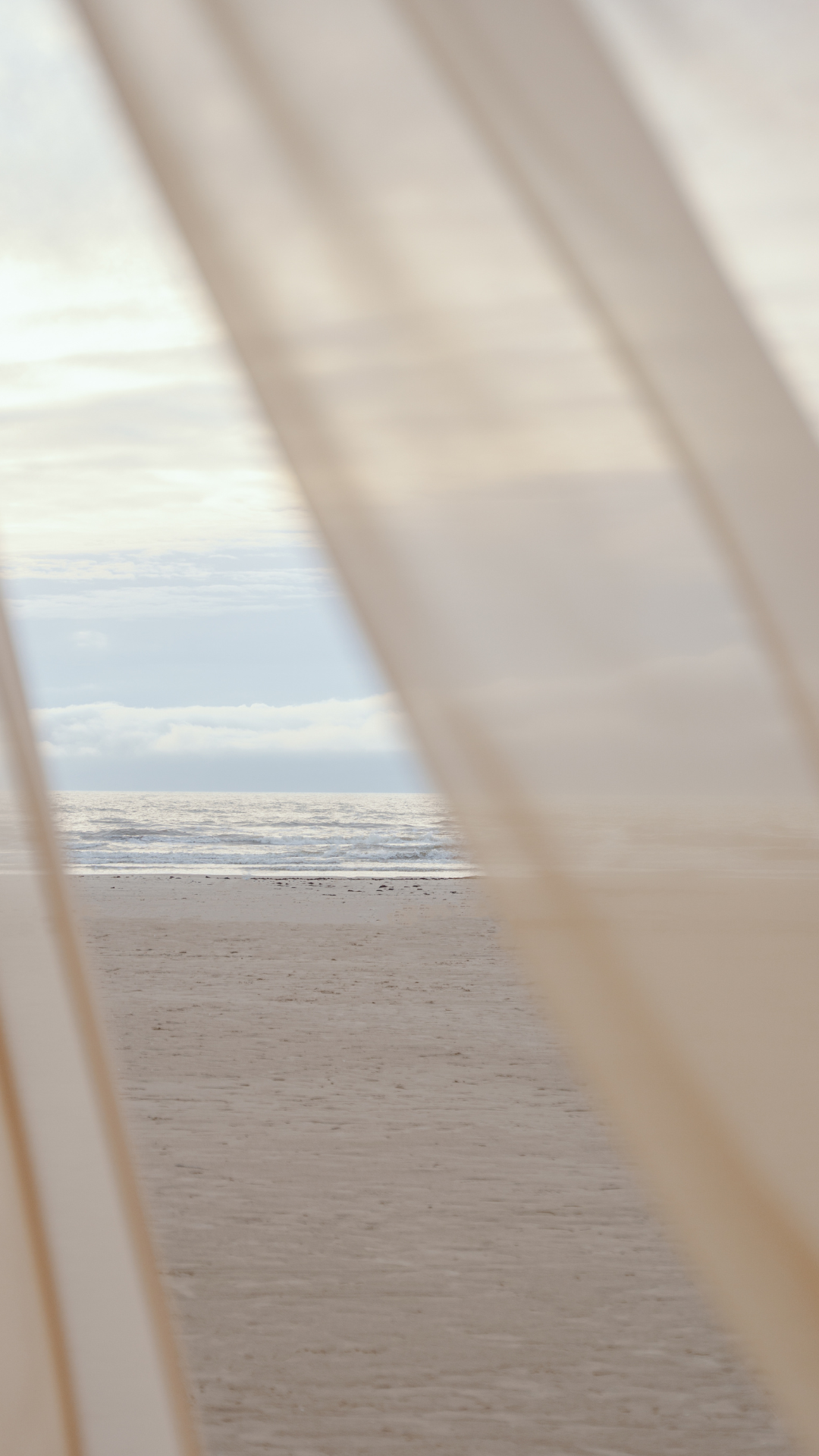 View of the beach and ocean through a partially open window or shutters.