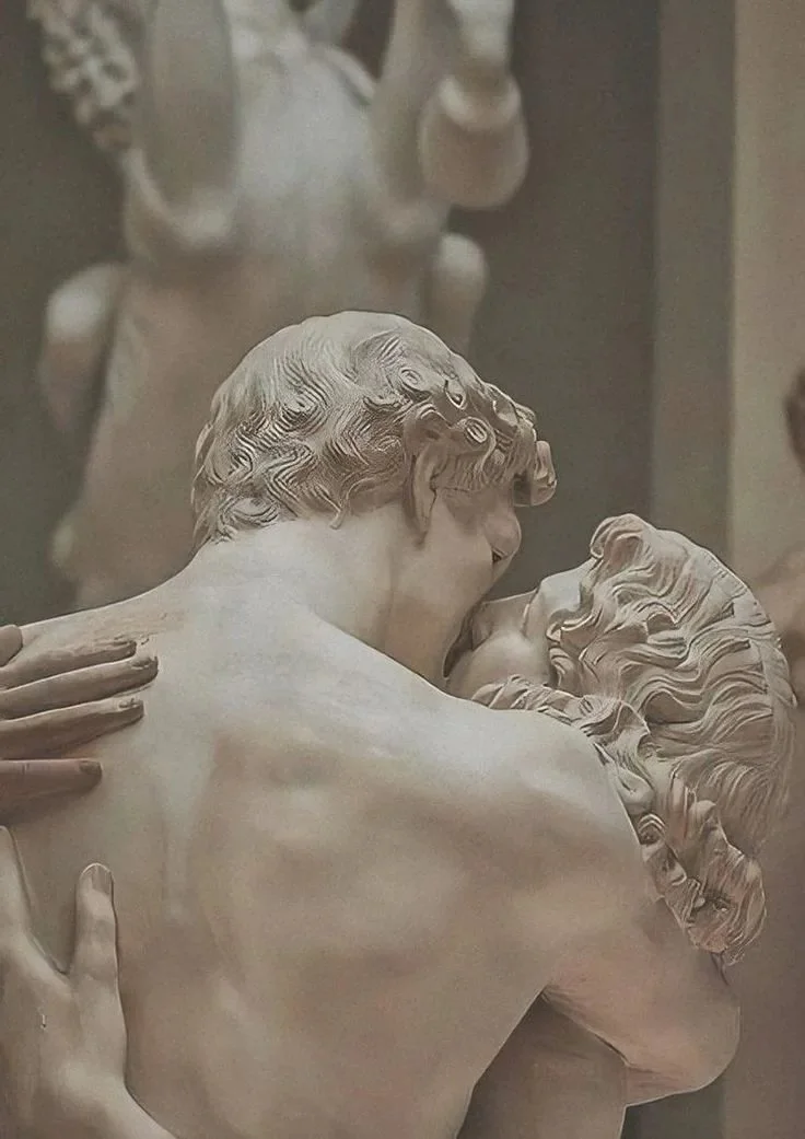 Close-up of a sculpture depicting two lovers embracing, with detailed curly hair and gentle expressions.