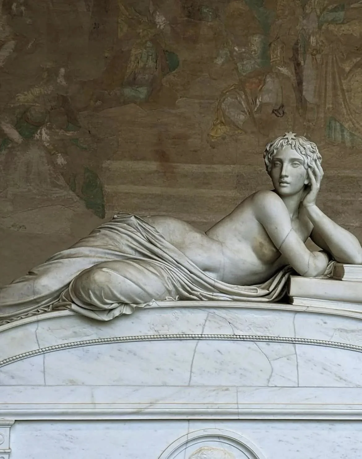Marble sculpture of a reclining woman with her head resting on her hand, lying on a curved base, with a background of faded Roman frescoes.
