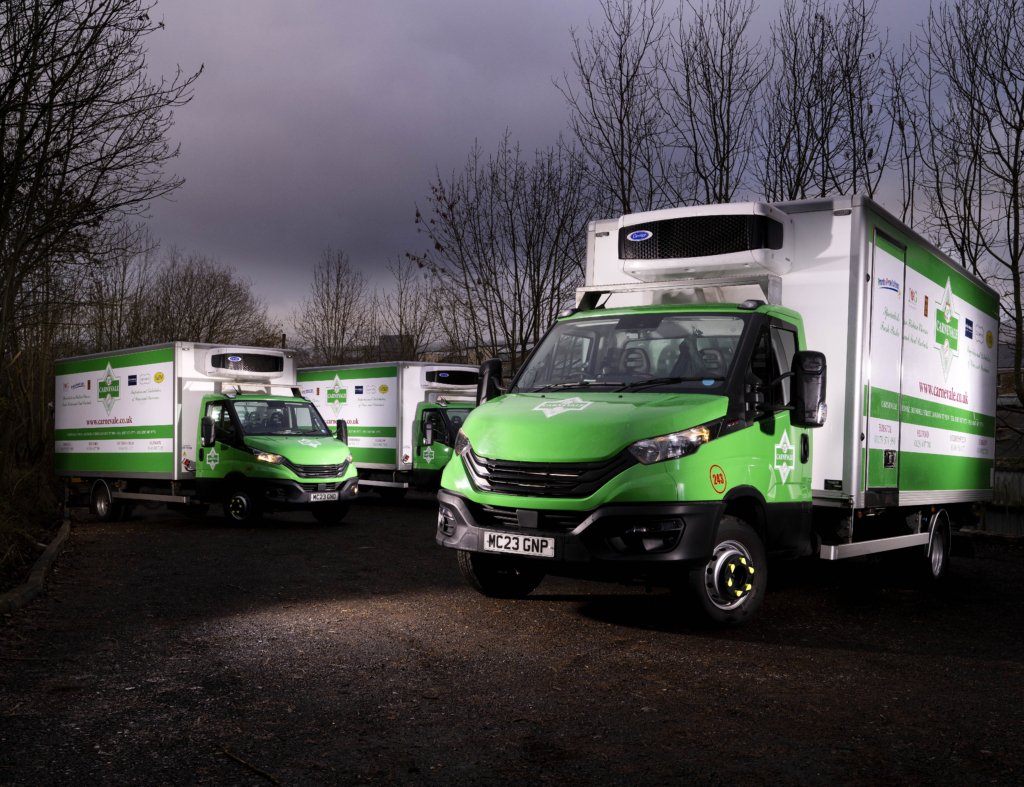 Three green and white delivery trucks parked outdoors on a cloudy day.
