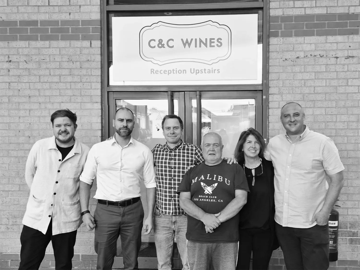 C&C Wine team standing in front of C&C Wines building with a sign that reads "C&C Wines, Reception Upstairs".