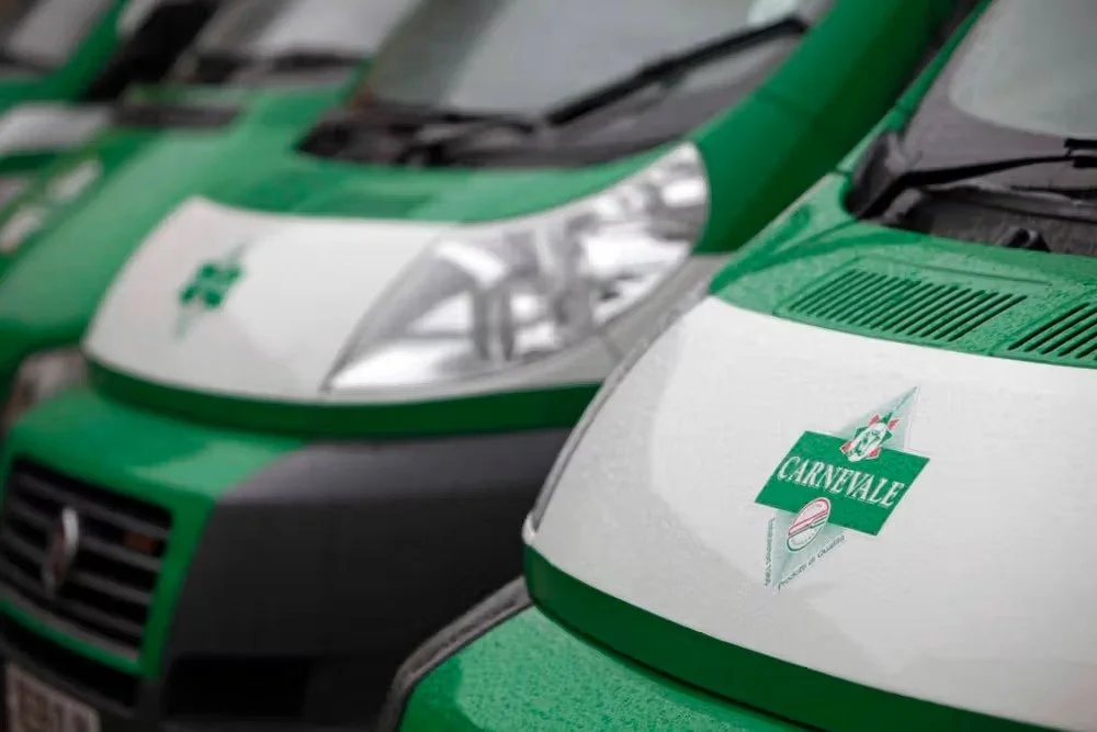Multiple green and white vehicles parked in a row, with a focus on the front of a vehicle displaying a 'Carnevale' sticker.