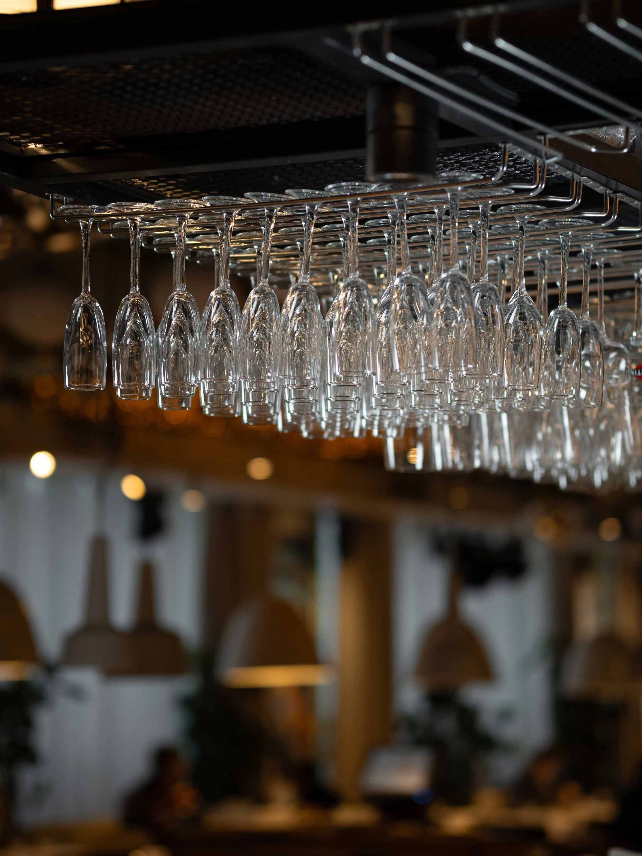 A row of upside-down wine glasses hanging from a rack inside a bar or restaurant.