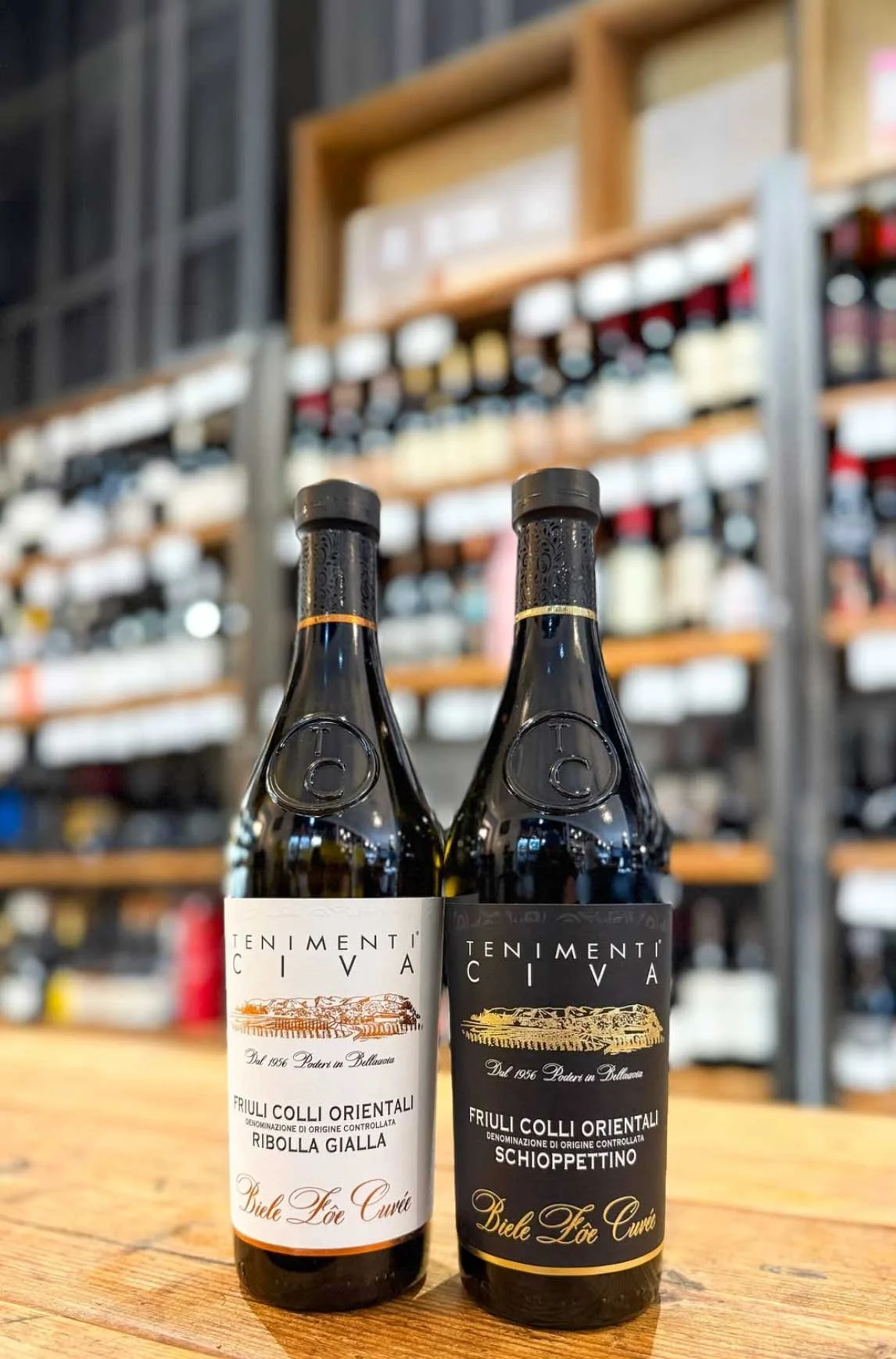 Two bottles of Italian wine standing on a wooden surface in front of a blurred background of wine shelves.