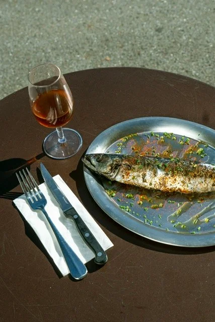 Poisson grillé servi sur un plat en métal, accompagné d'un verre de vin rosé et d'ustensiles de table posés sur une nappe blanche
