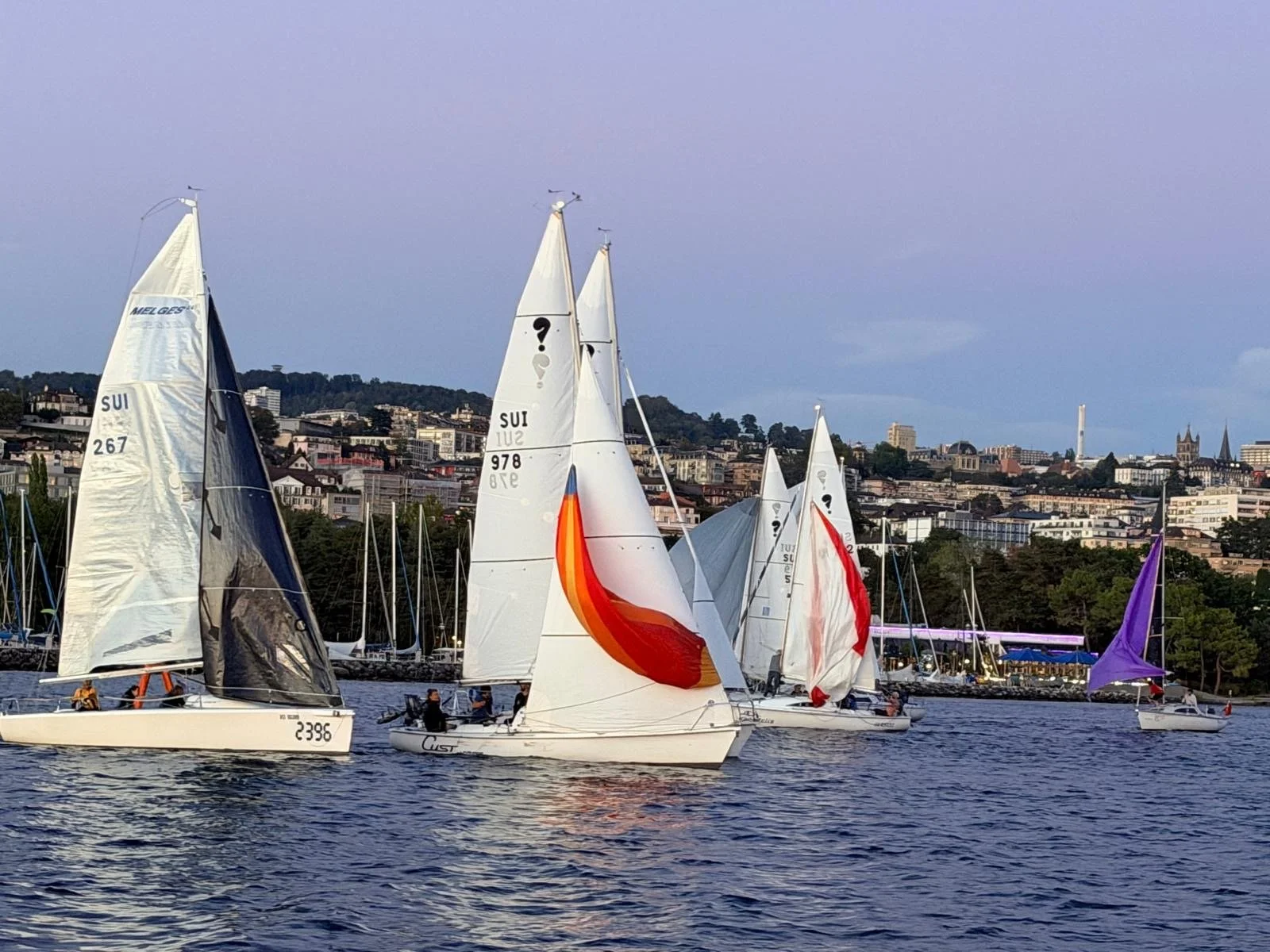 Voiliers de course sur un lac avec une ville en arrière-plan, ciel clair