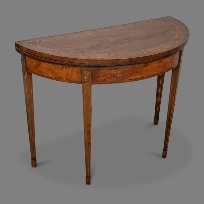 An antique wooden half-moon console table with four tapered legs and decorative floral inlay on the apron, on a gray background.
