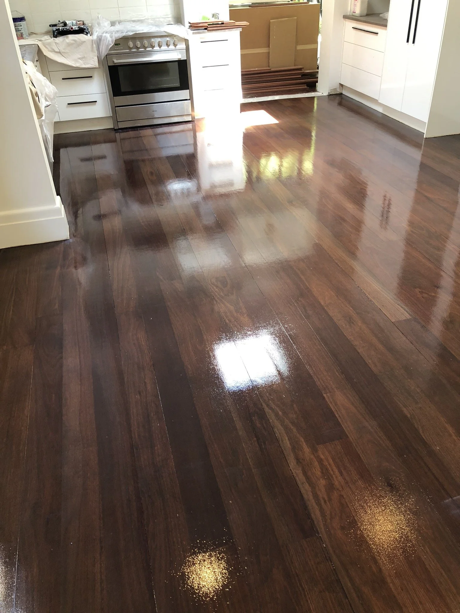 Wooden floor being polished in a kitchen space with white cabinets and a stainless steel stove.