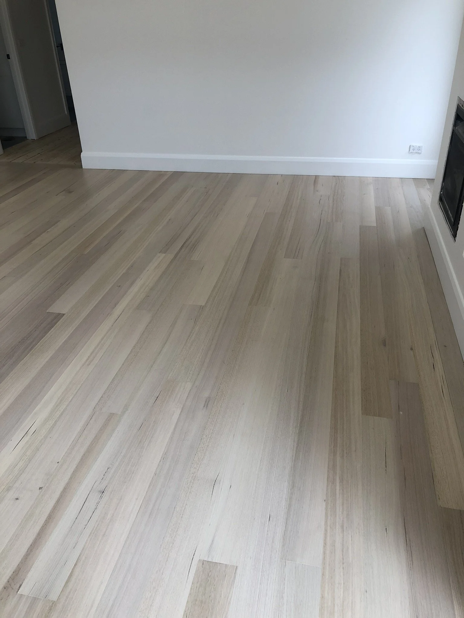 Empty room with light wood flooring, white walls, and a corner electrical outlet.