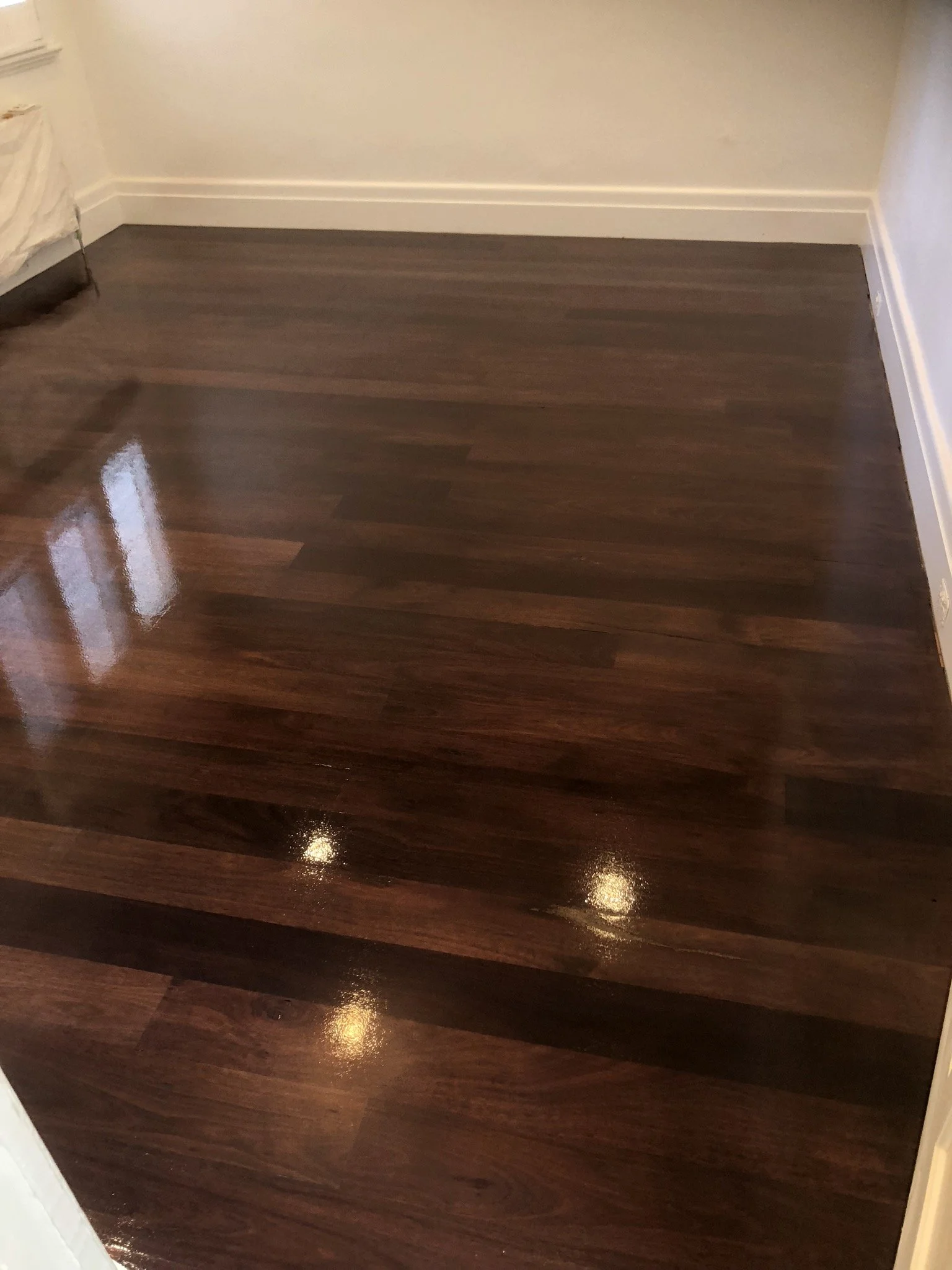 Freshly polished dark wood floor in a corner of a room with beige walls and white baseboards.