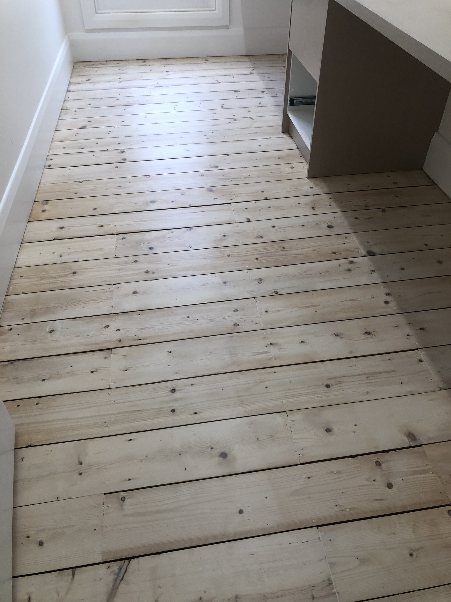 Wooden floor with light-colored planks in a room near a door and a light-colored wall.