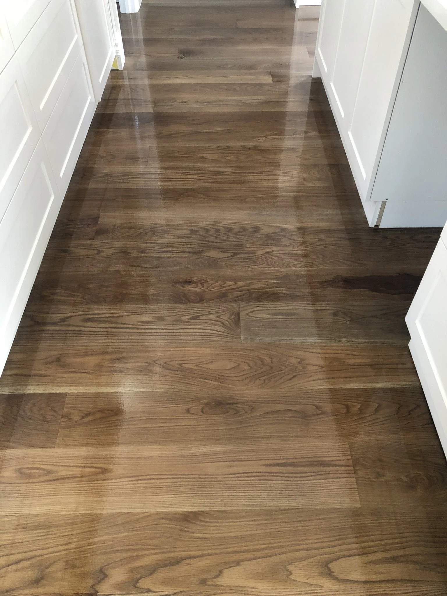 Shiny wooden kitchen floor with white cabinets and drawers on both sides.