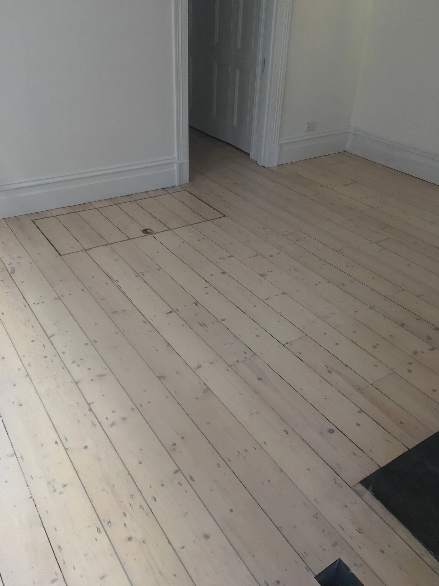 Wooden floor in a room with an access hatch near a door.