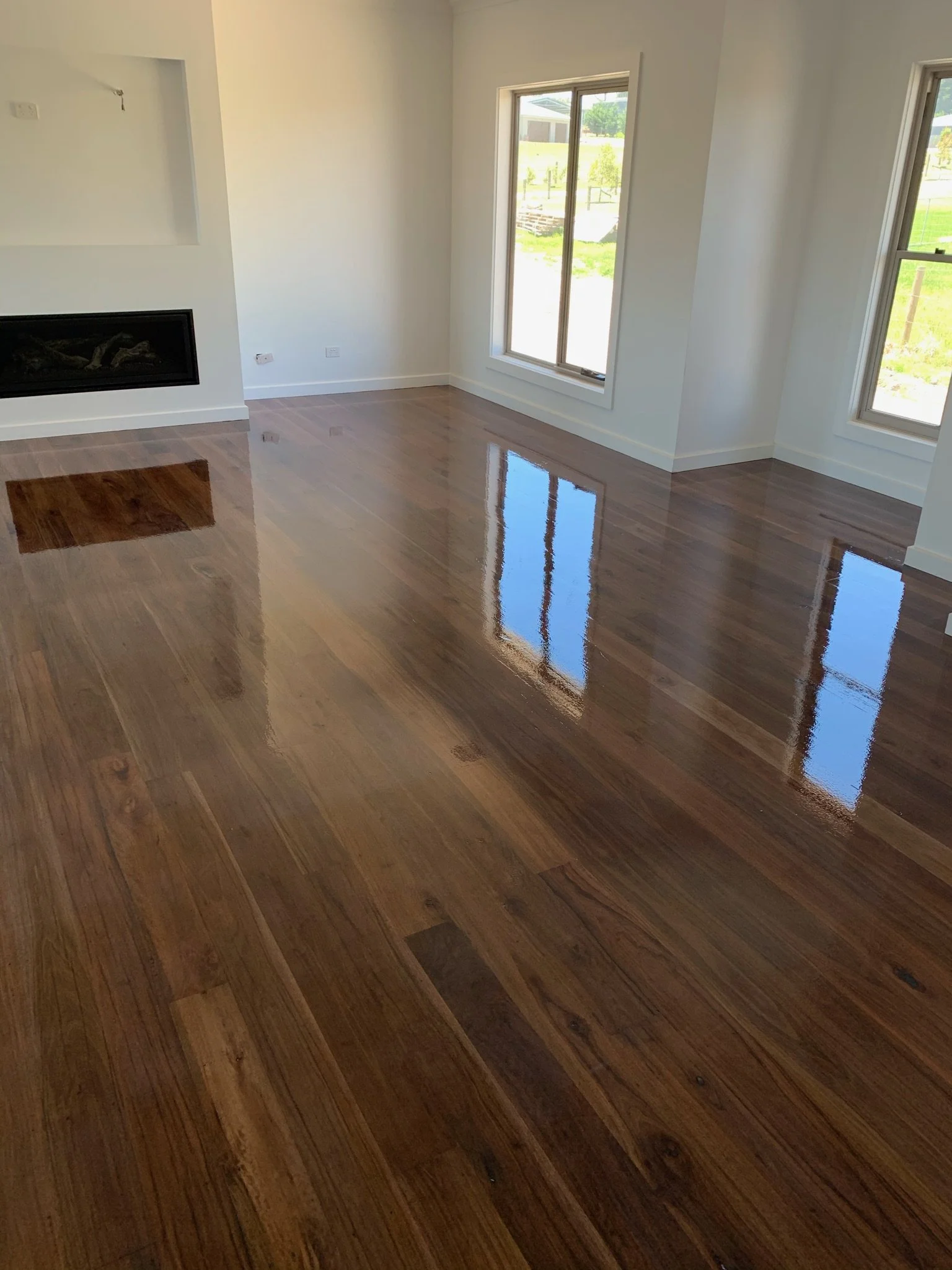Empty living room with hardwood floors and large windows showing a grassy outdoor area.