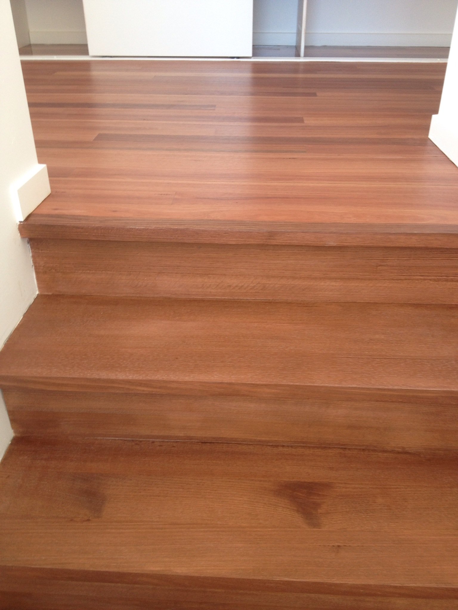 Wooden stairs leading up to a doorway with a white door and white wall on the sides.
