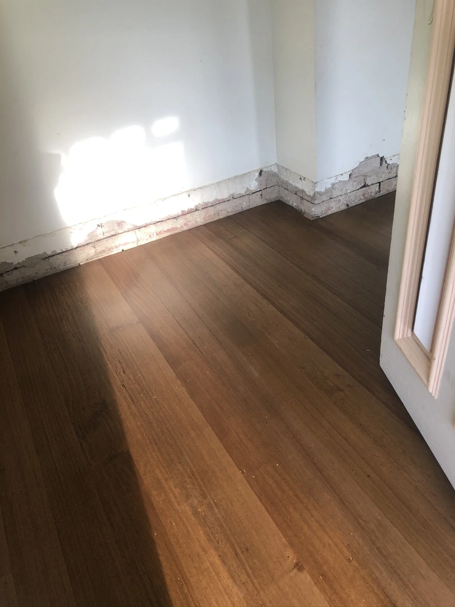 Close-up of a partly demolished wall corner with exposed bricks at the base, next to a wooden floor with a dark stain.