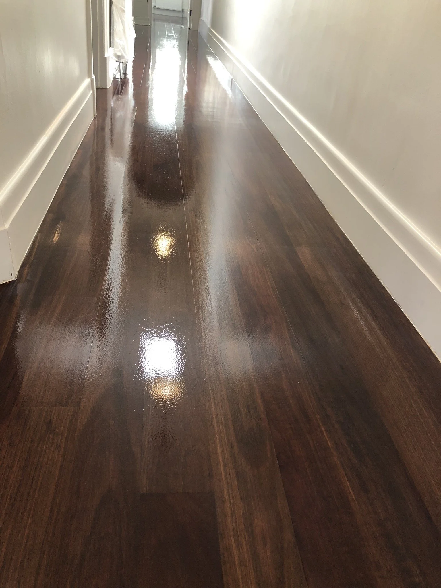 Polished, shiny wooden floor in a hallway with white baseboards and a beige wall.