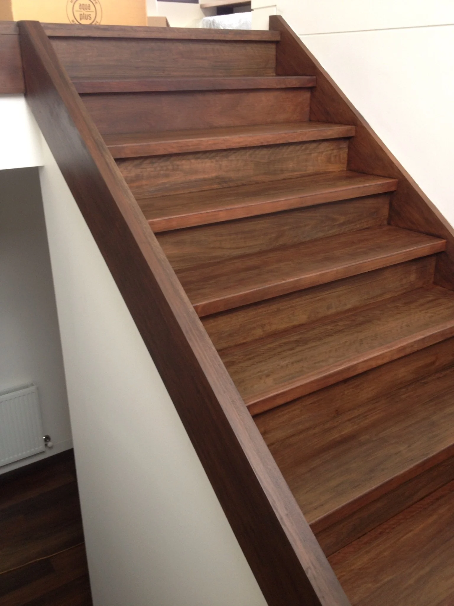 Wooden staircase with dark brown stairs and matching handrail, adjacent to a white wall.