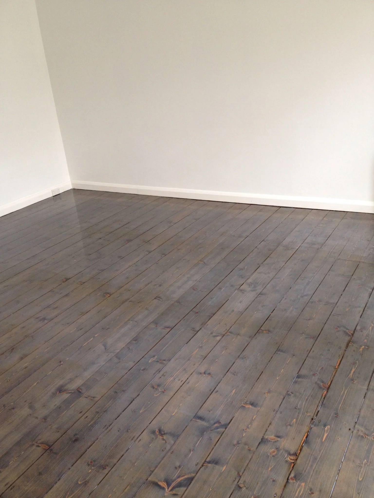 Empty room with white walls and dark wooden plank flooring.