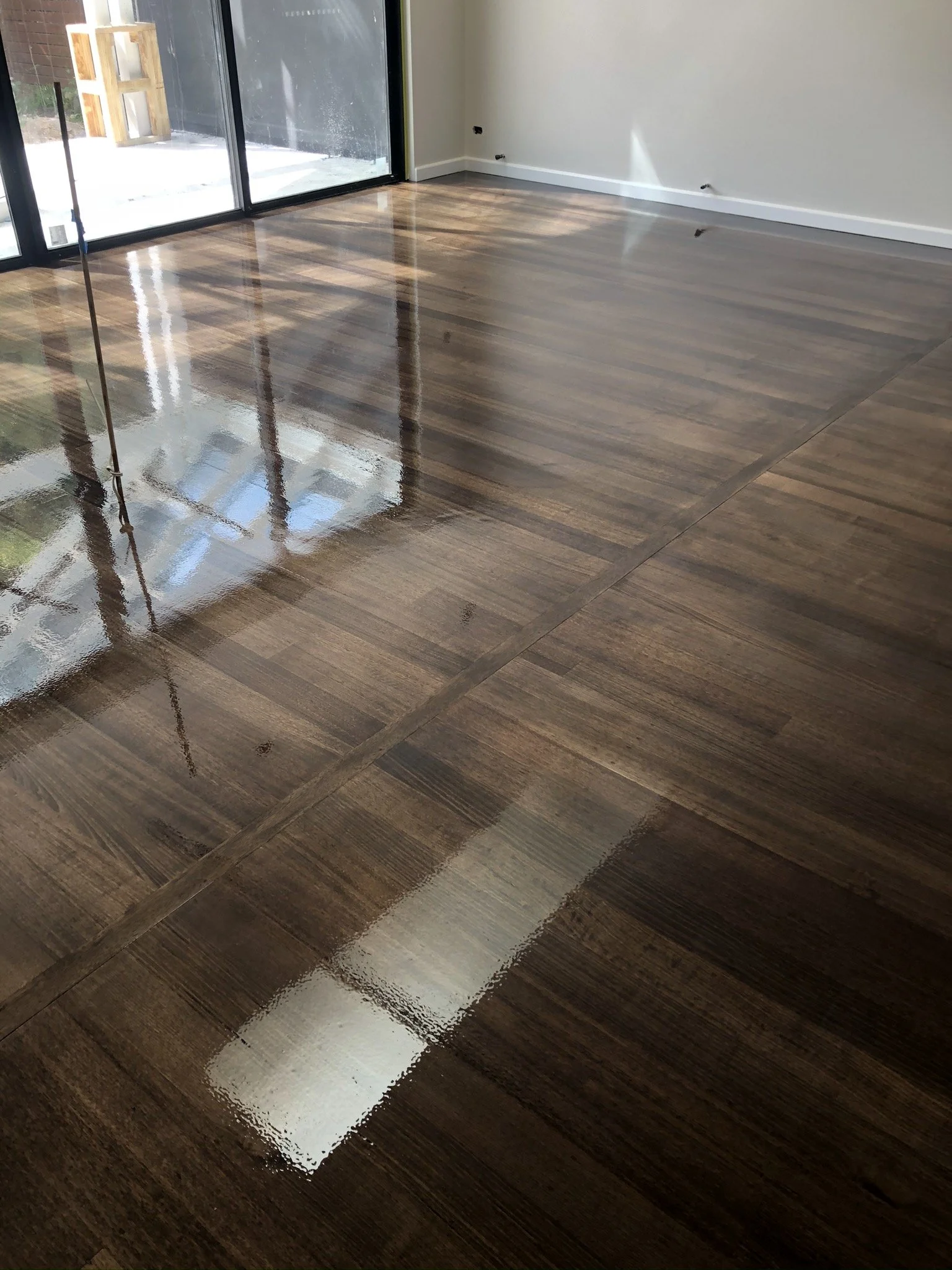 Shiny, freshly polished hardwood floor in a modern room with large sliding glass doors and white walls.