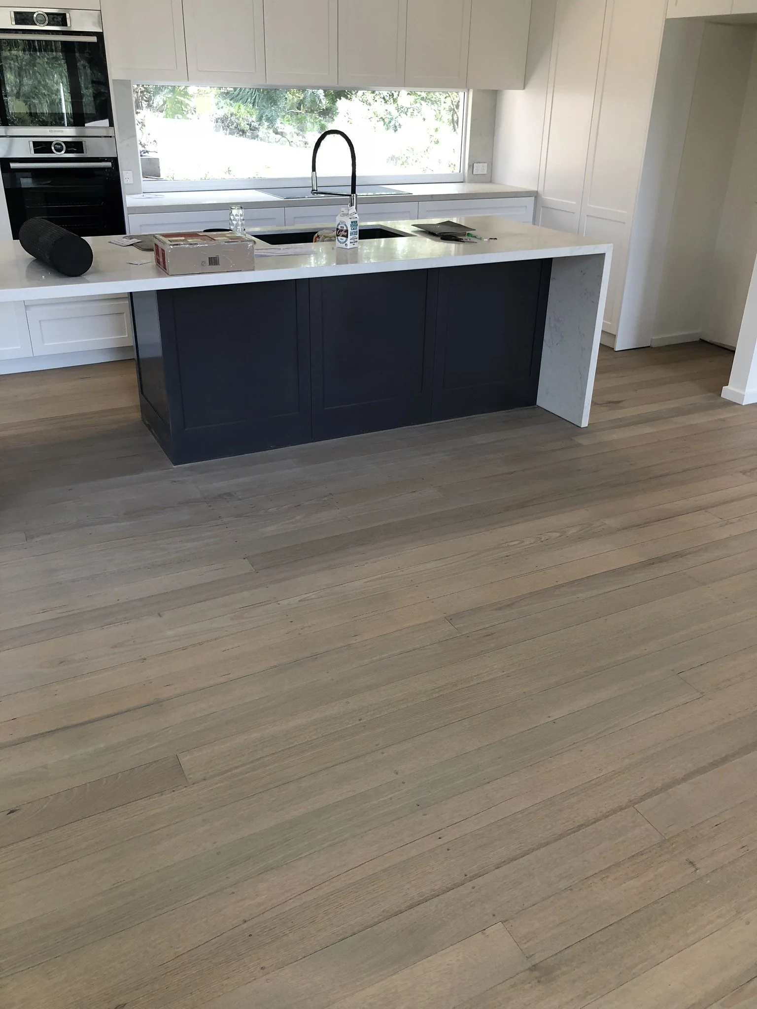 Modern kitchen with a black island counter, a white marble countertop, a sink, a faucet, and light-colored wooden floors.
