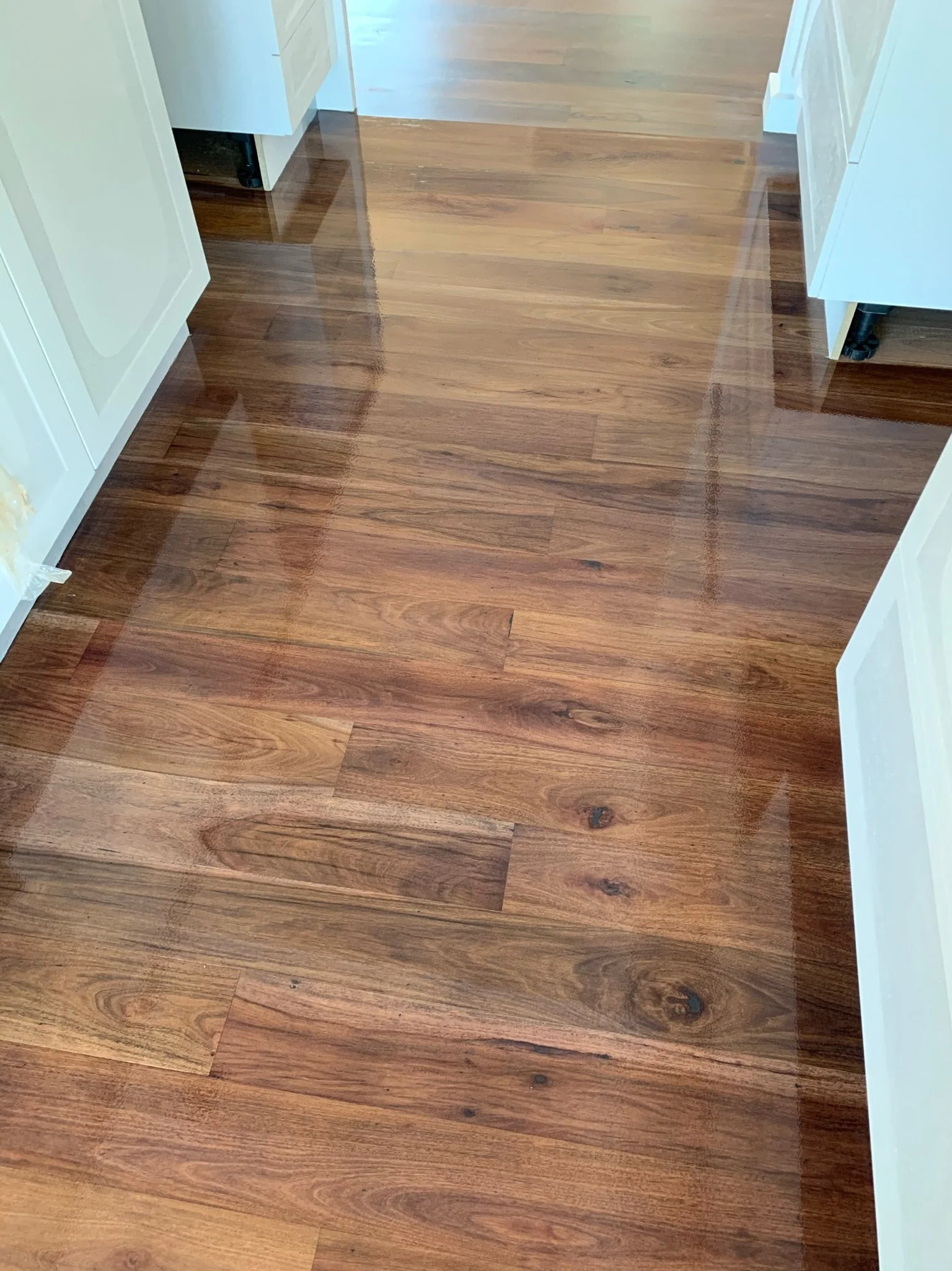 Polished wooden floor in a hallway or kitchen area, surrounded by white cabinets and trim.