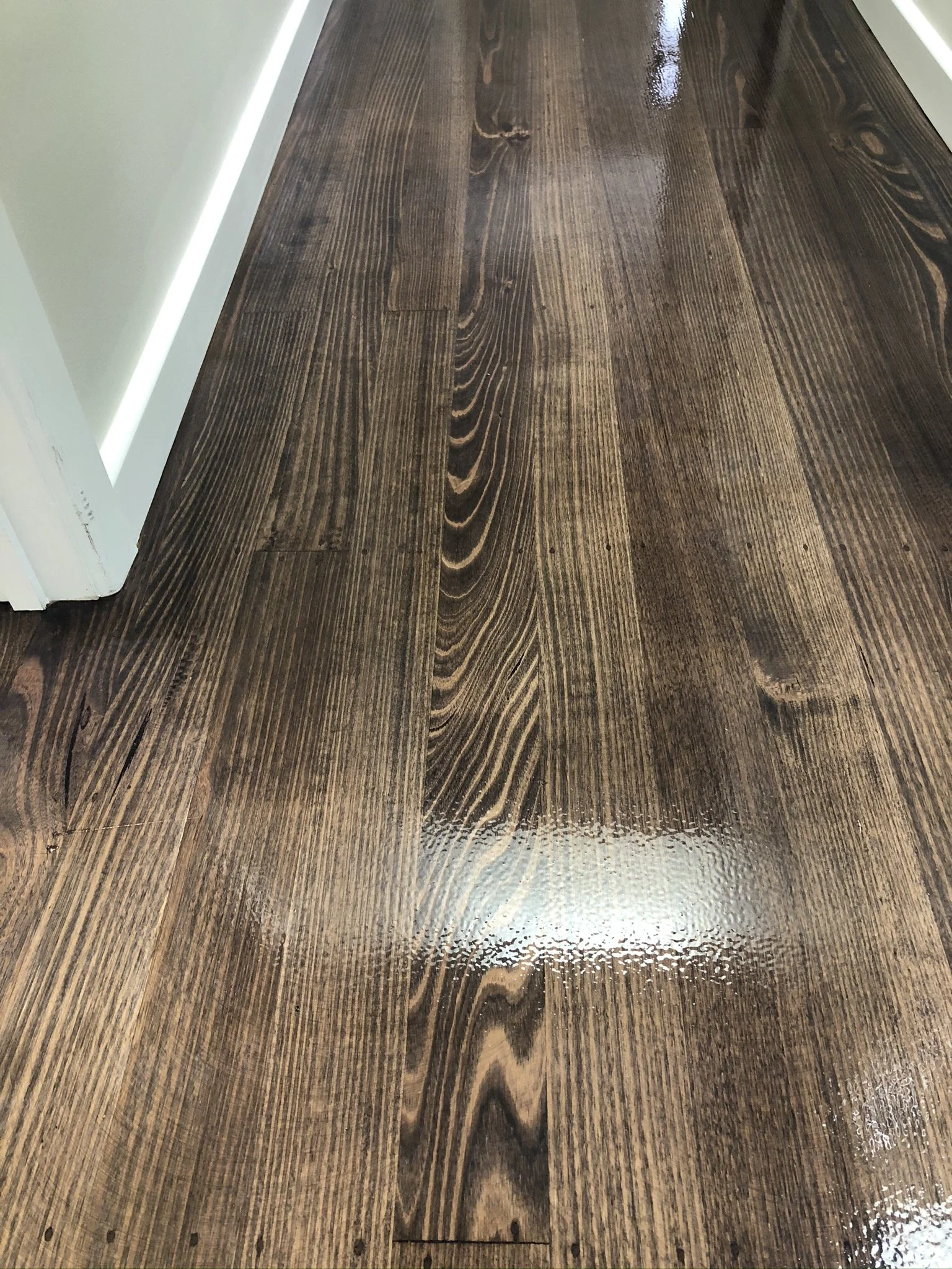 Shiny, dark-stained hardwood floors next to a white door and beige wall.