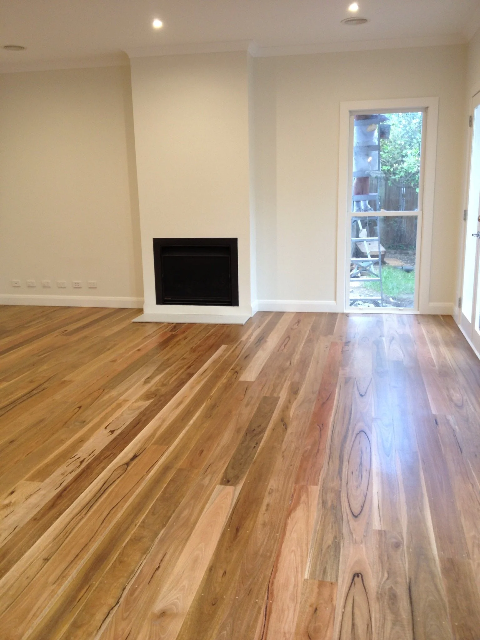 Living room with polished hardwood floors, a fireplace, a glass door leading outside, and beige walls.