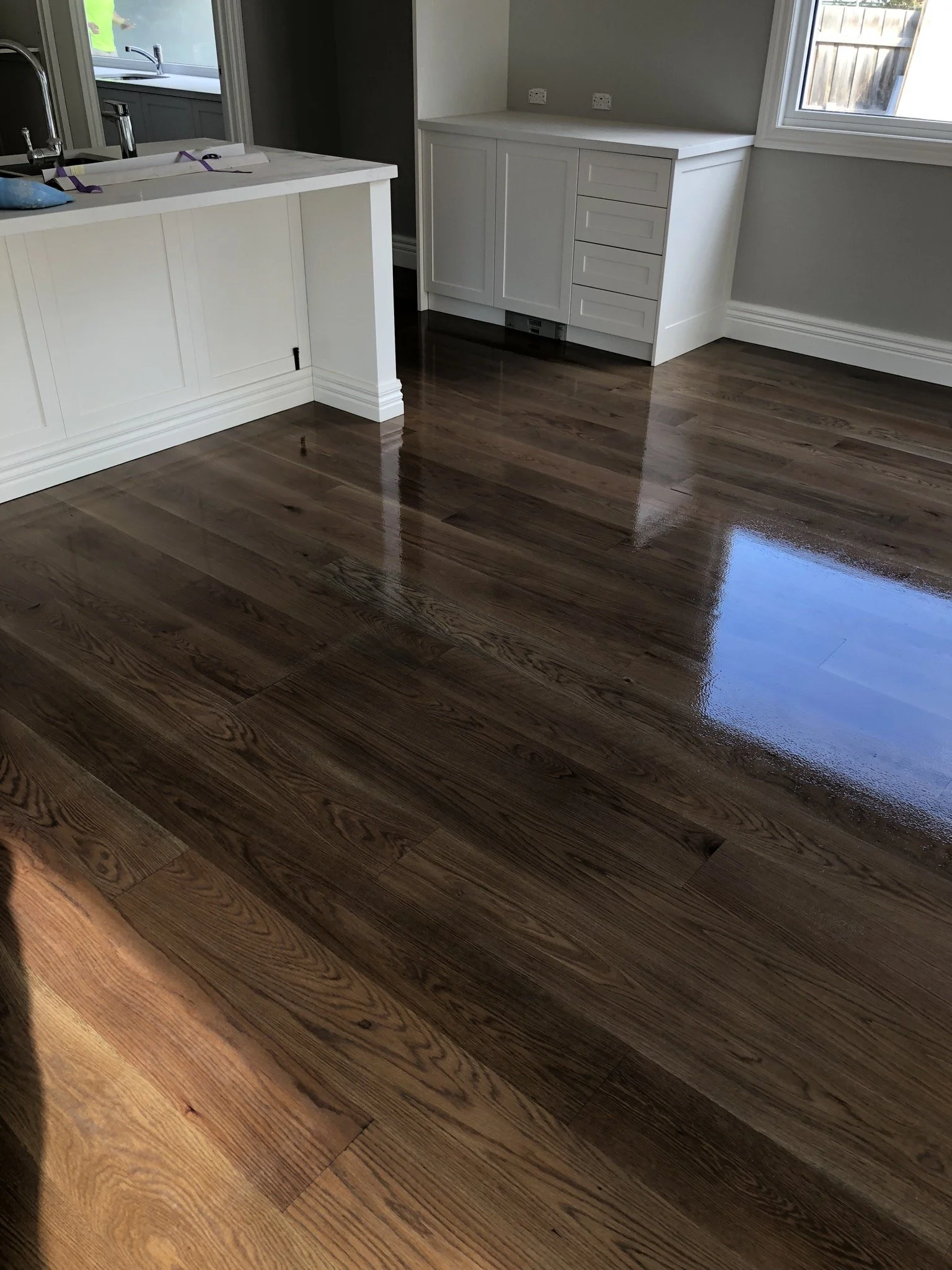 Interior view of a room with polished hardwood floors, white cabinetry, and a window letting in natural light.