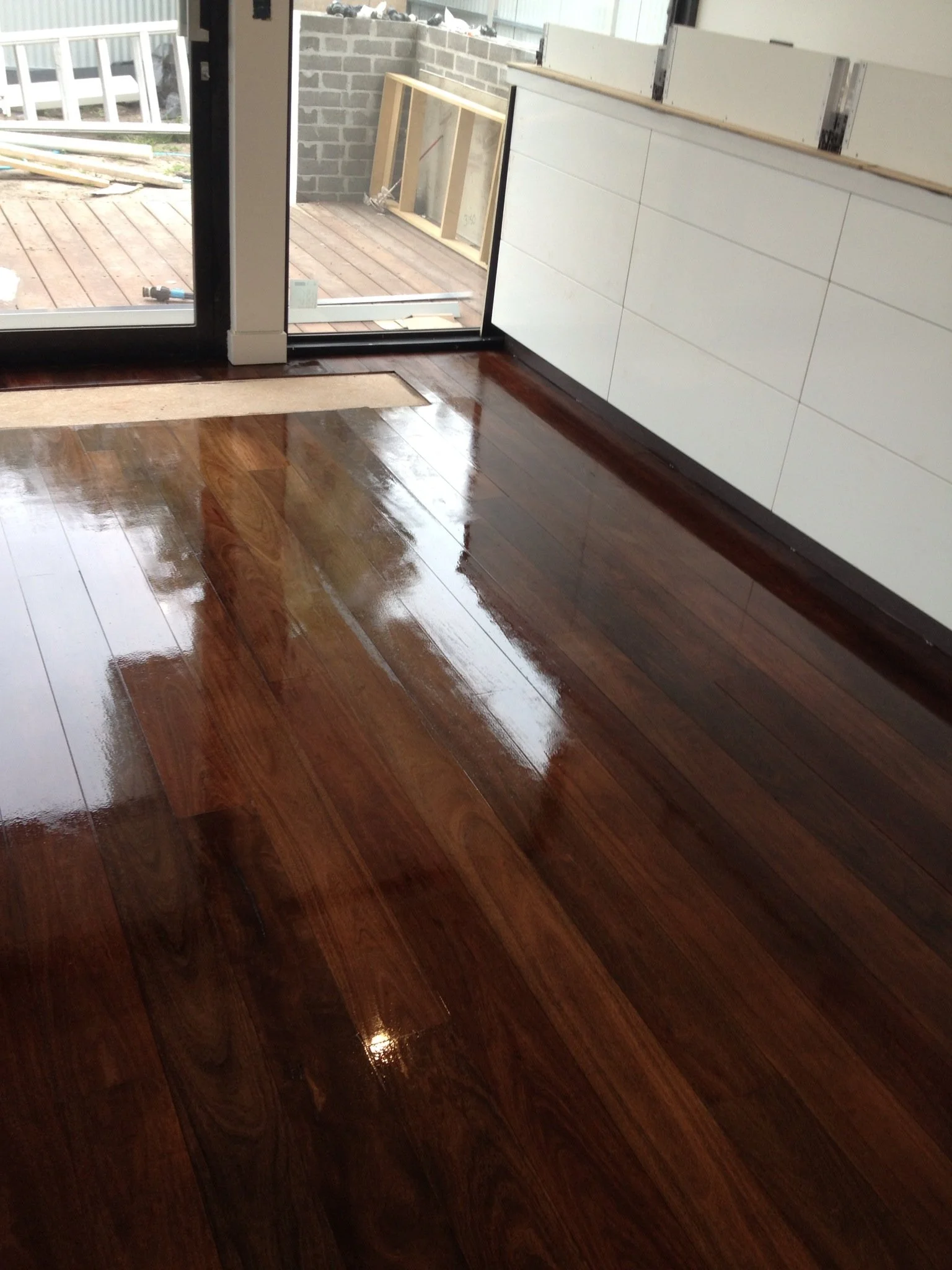 Freshly polished dark hardwood floor in a modern kitchen with sliding glass door and outdoor deck visible