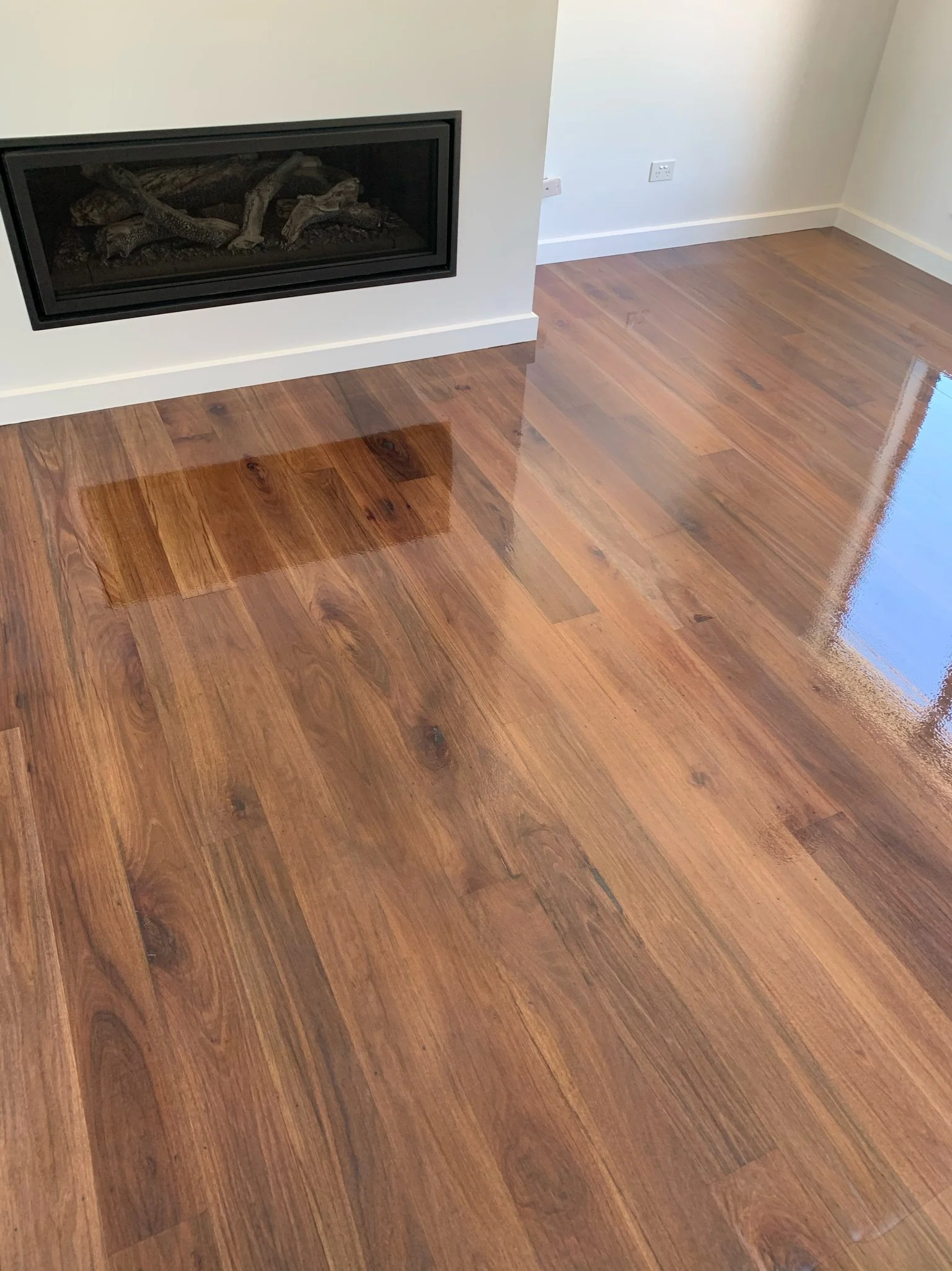 A room with polished, glossy hardwood floor and a modern fireplace on the wall.