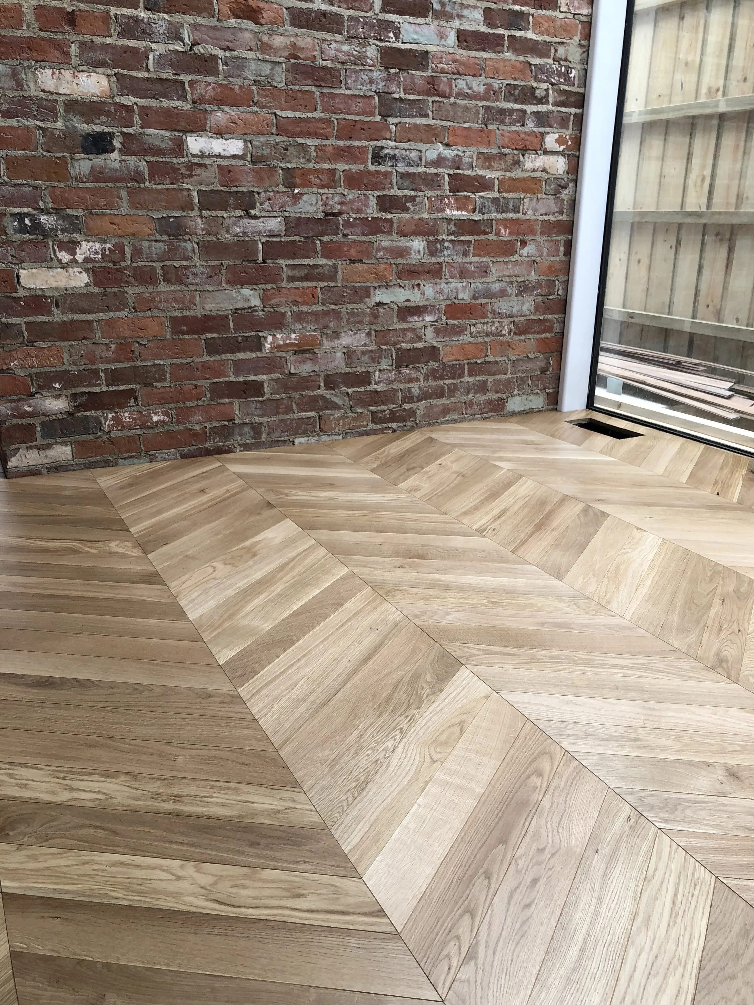 Interior with a red brick wall, wooden chevron-patterned flooring, and a glass door leading to an outdoor space.