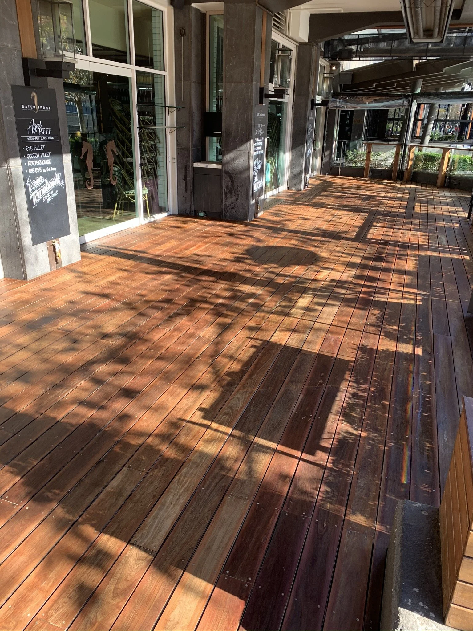 Empty outdoor wooden deck with chair shadows and sunlight.