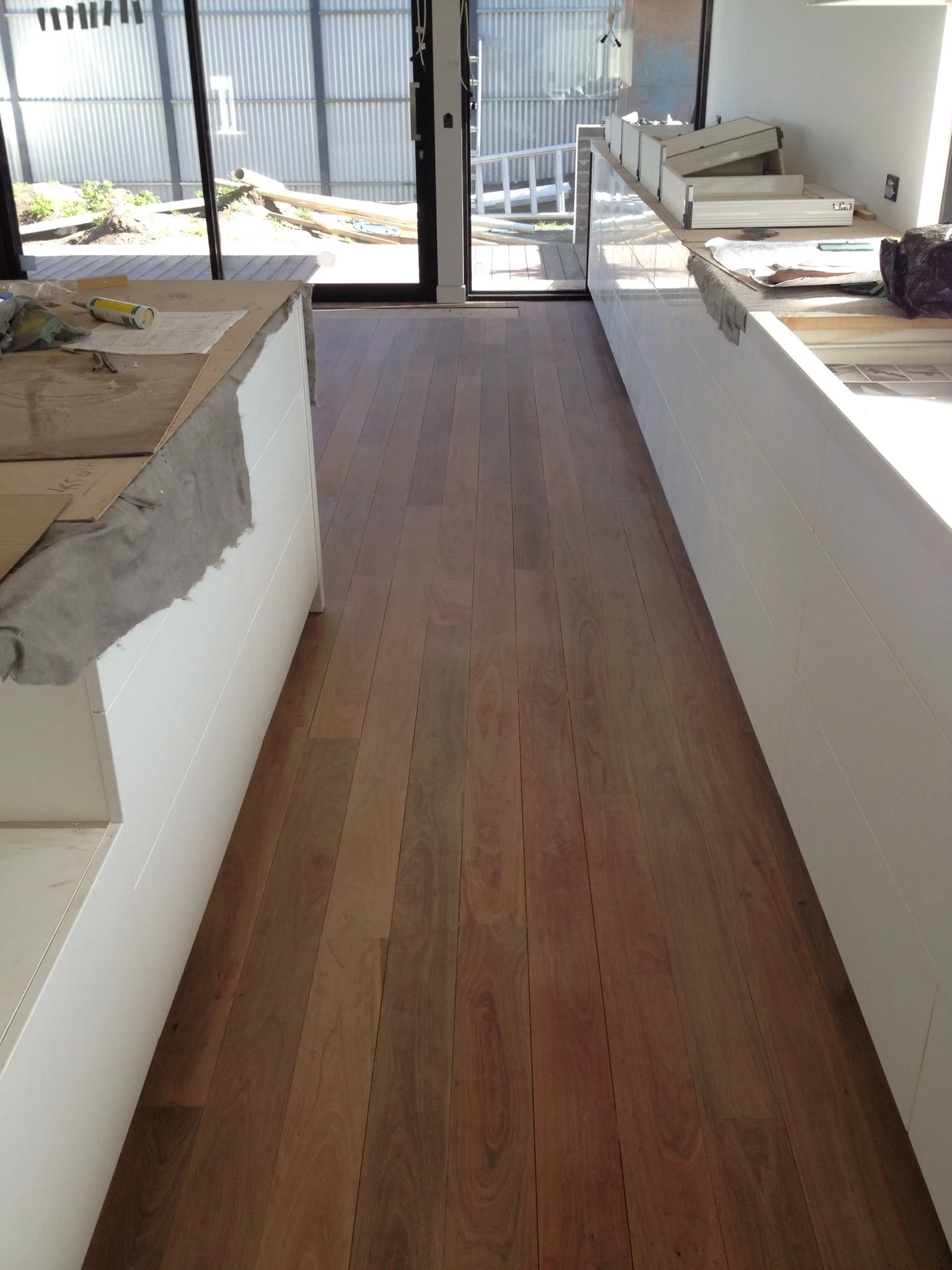 A kitchen under construction with hardwood flooring, white cabinetry, and sliding glass doors leading to an outdoor deck.