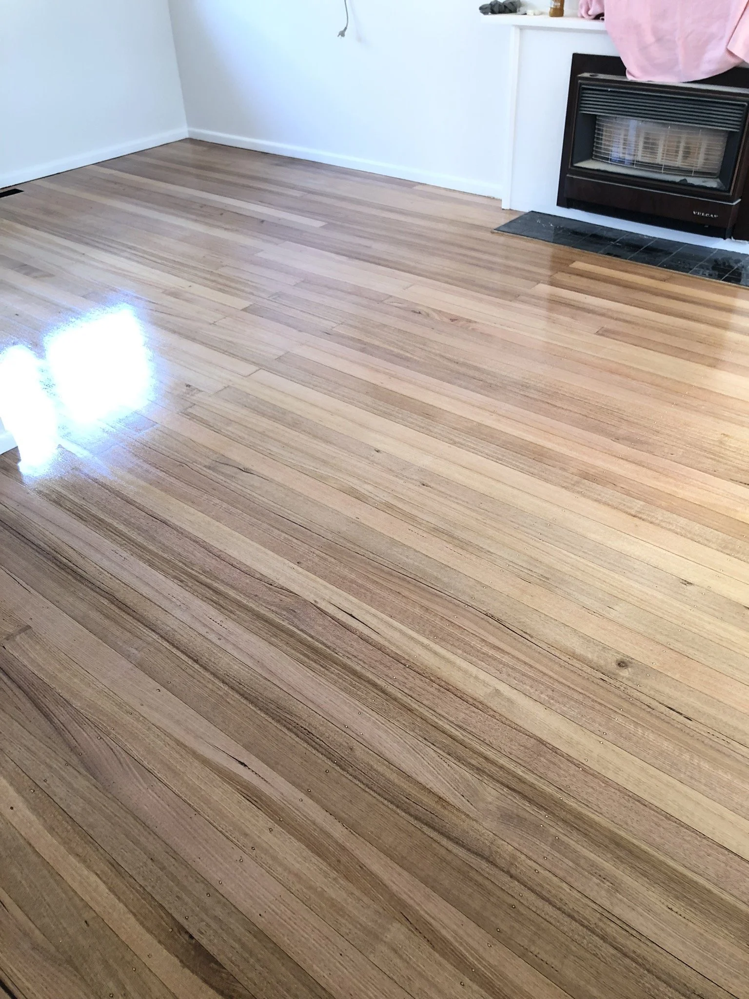 Empty room with a hardwood floor, white walls, fireplace, and some items on the mantel.