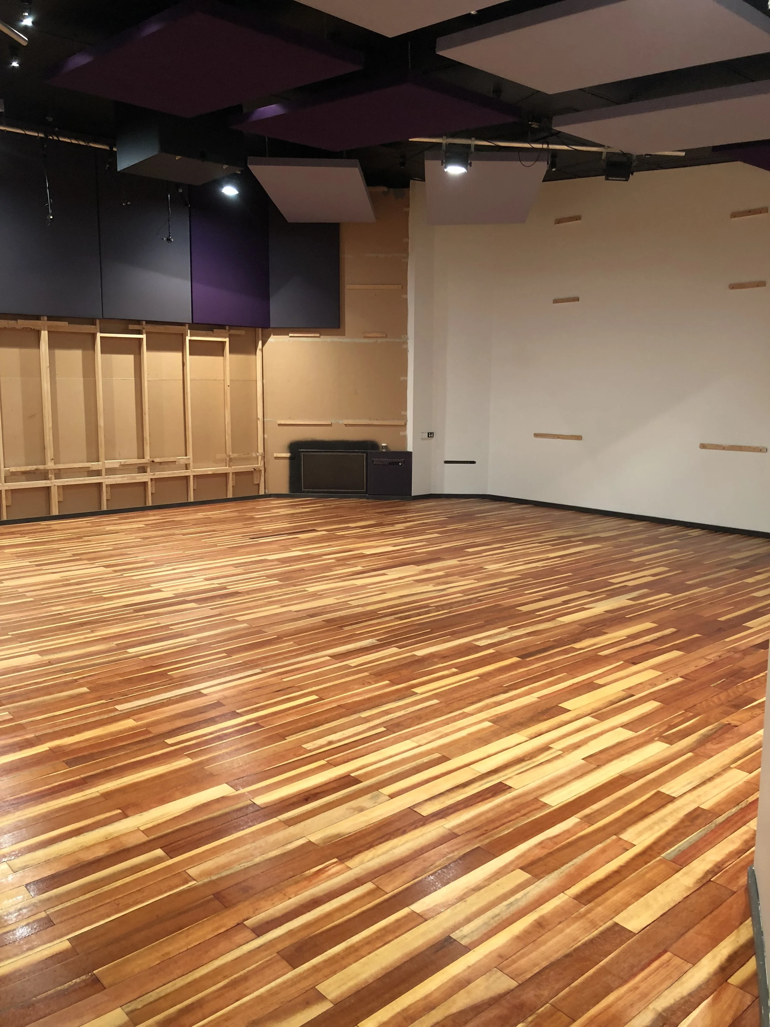 Empty room with polished wooden floor and covered soundproof ceiling panels, possibly a recording studio or performance space.