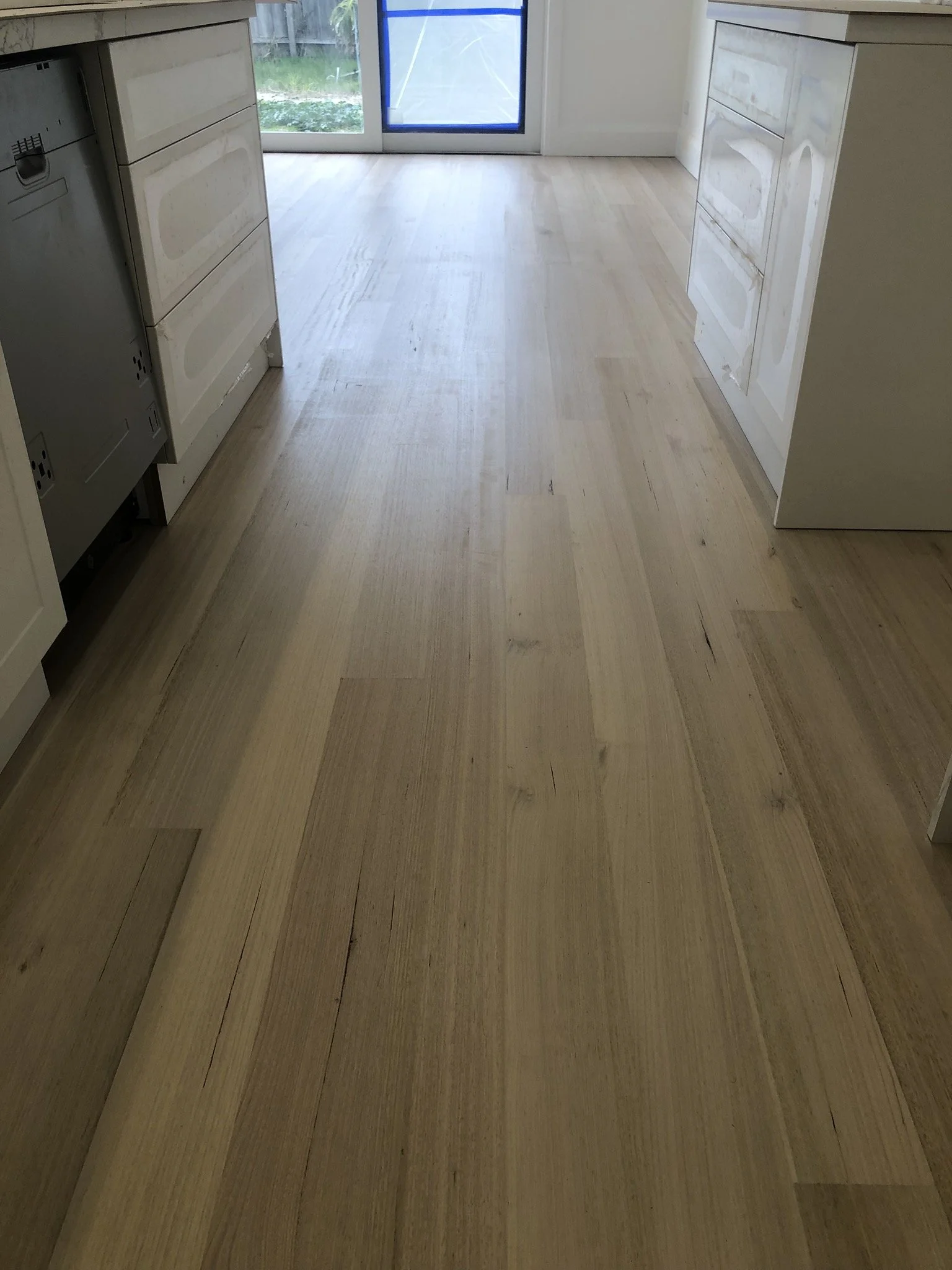 Wooden kitchen floor with white cabinets on both sides and a glass door at the back leading to a backyard.