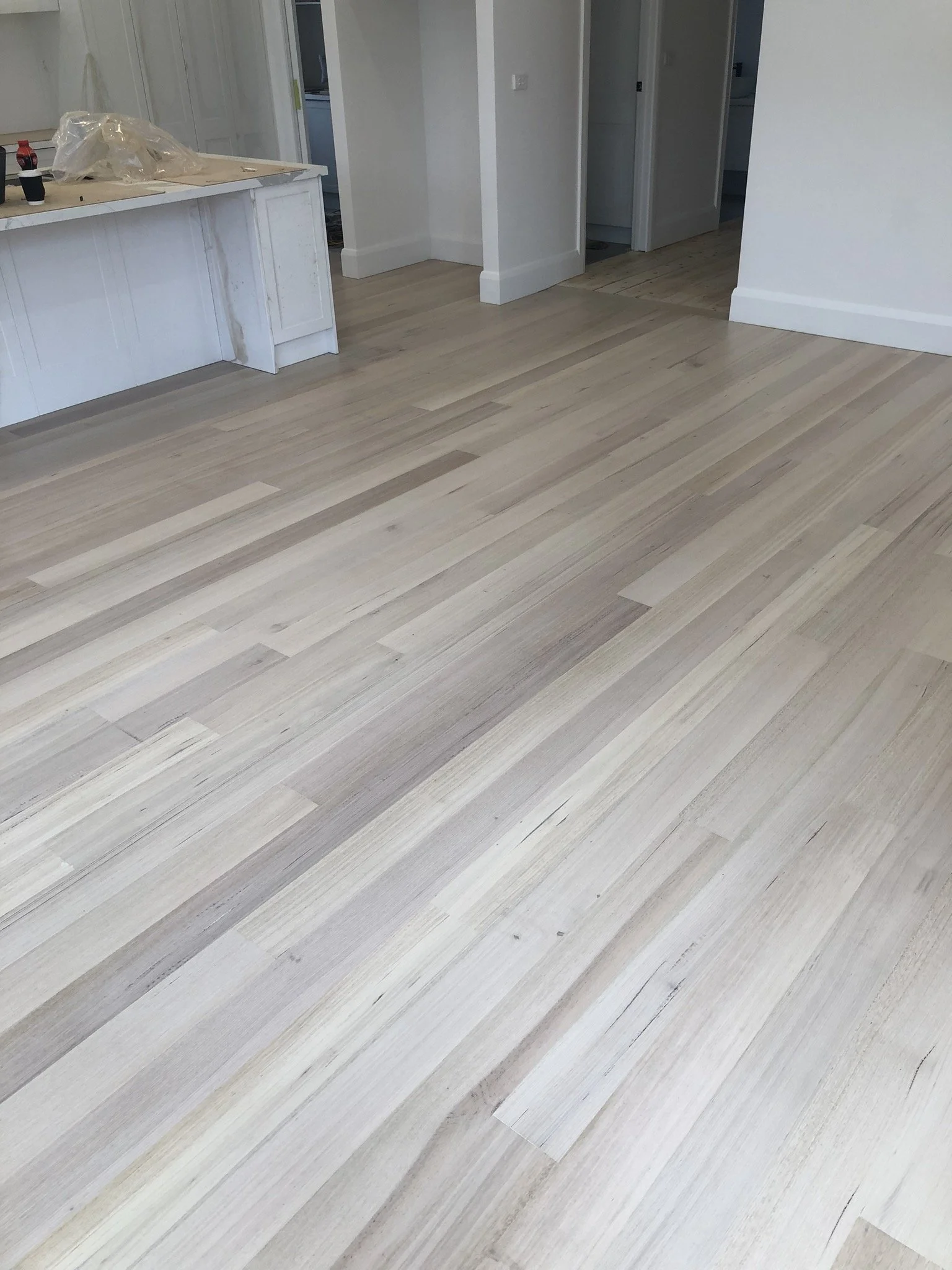 Light-colored hardwood flooring in a room, with some construction materials and tools on a white counter in the background.