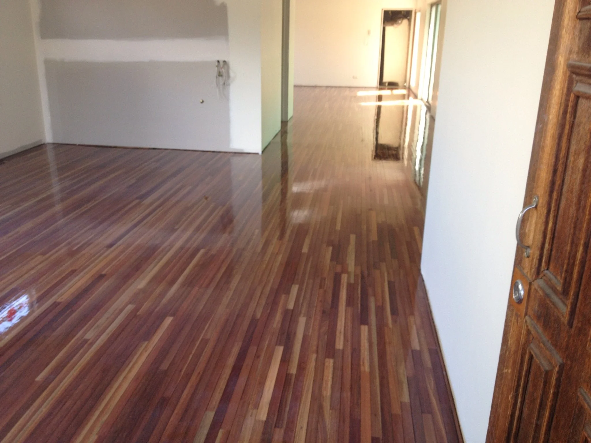 Living room with newly finished hardwood floors and white walls, with an open layout leading to a hallway and balcony door.