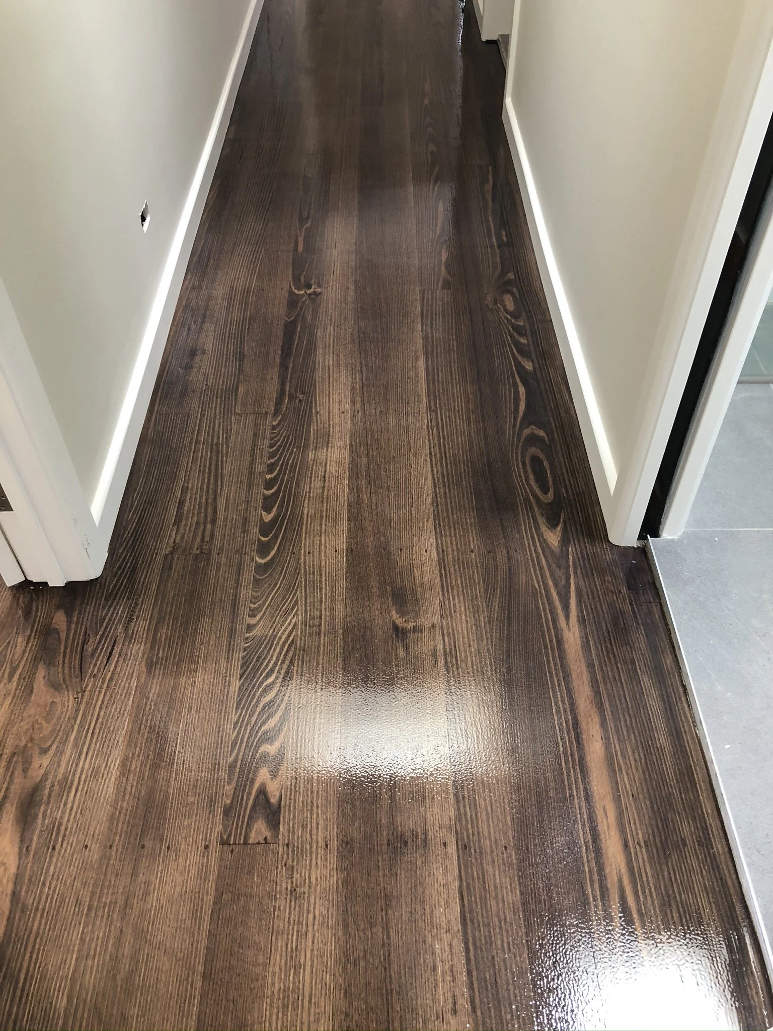 A hallway with dark stained wooden flooring, cream-colored walls, and white baseboards.