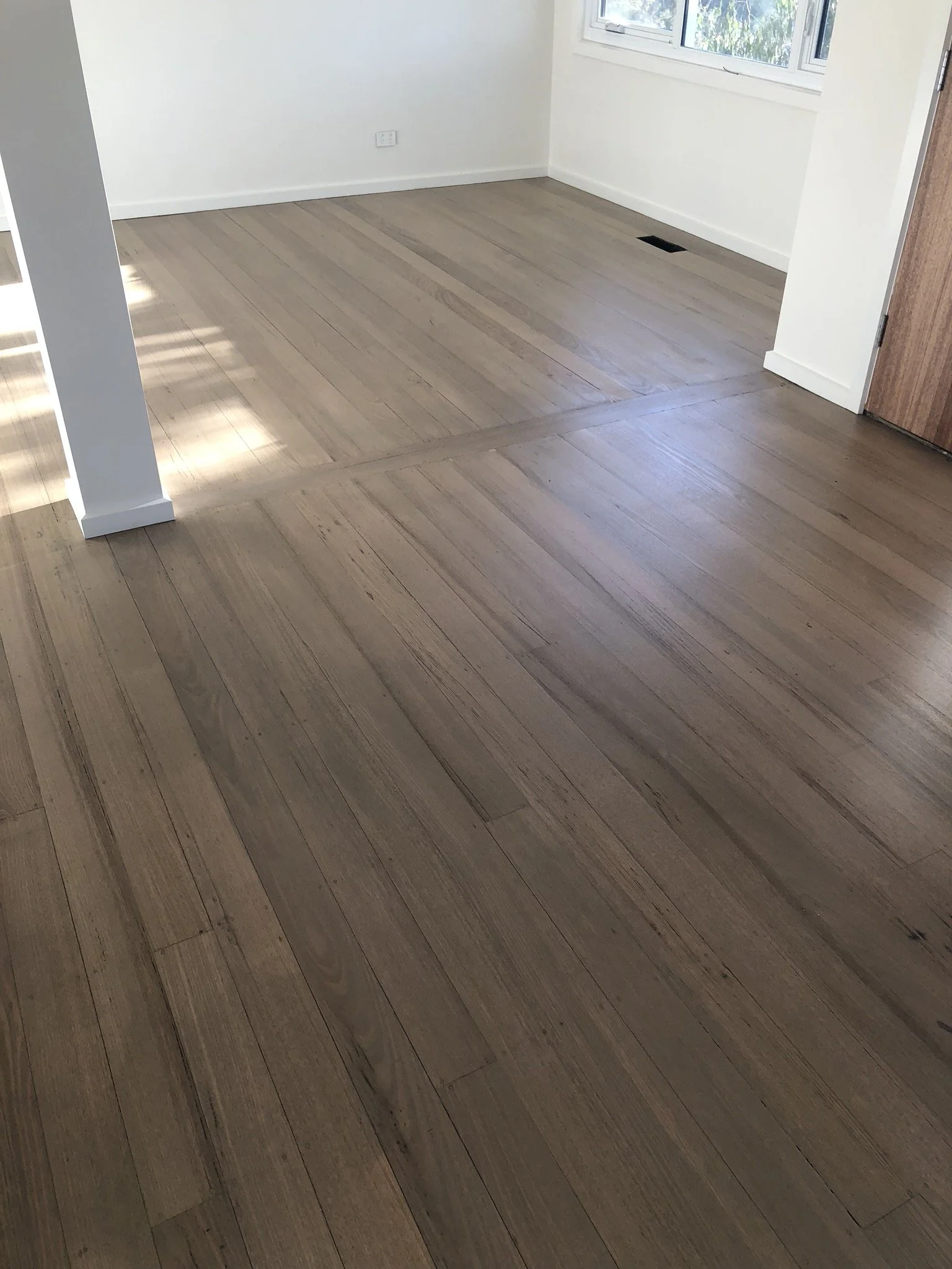 Empty room with newly installed wooden floorboards, white walls, a window, and a door.
