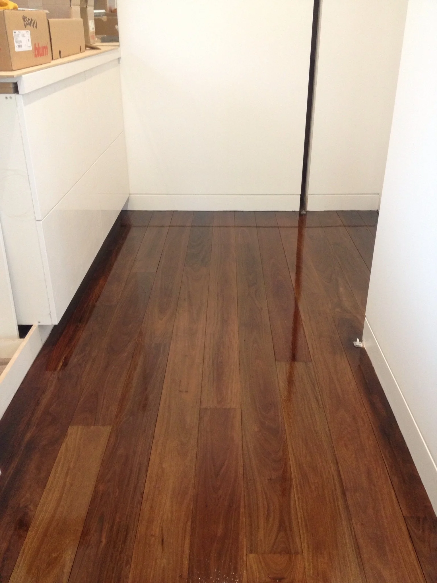 A wooden floored room with white walls, a white door, and a white countertop with cardboard boxes on it.