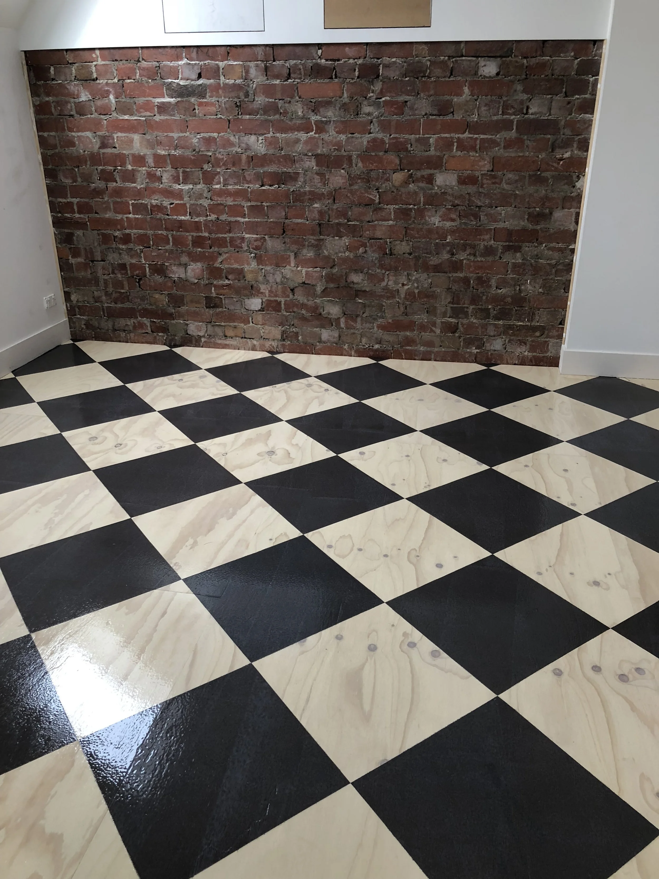 Room with black and cream checkered flooring, exposed red brick wall, and white walls with wood panel accents.