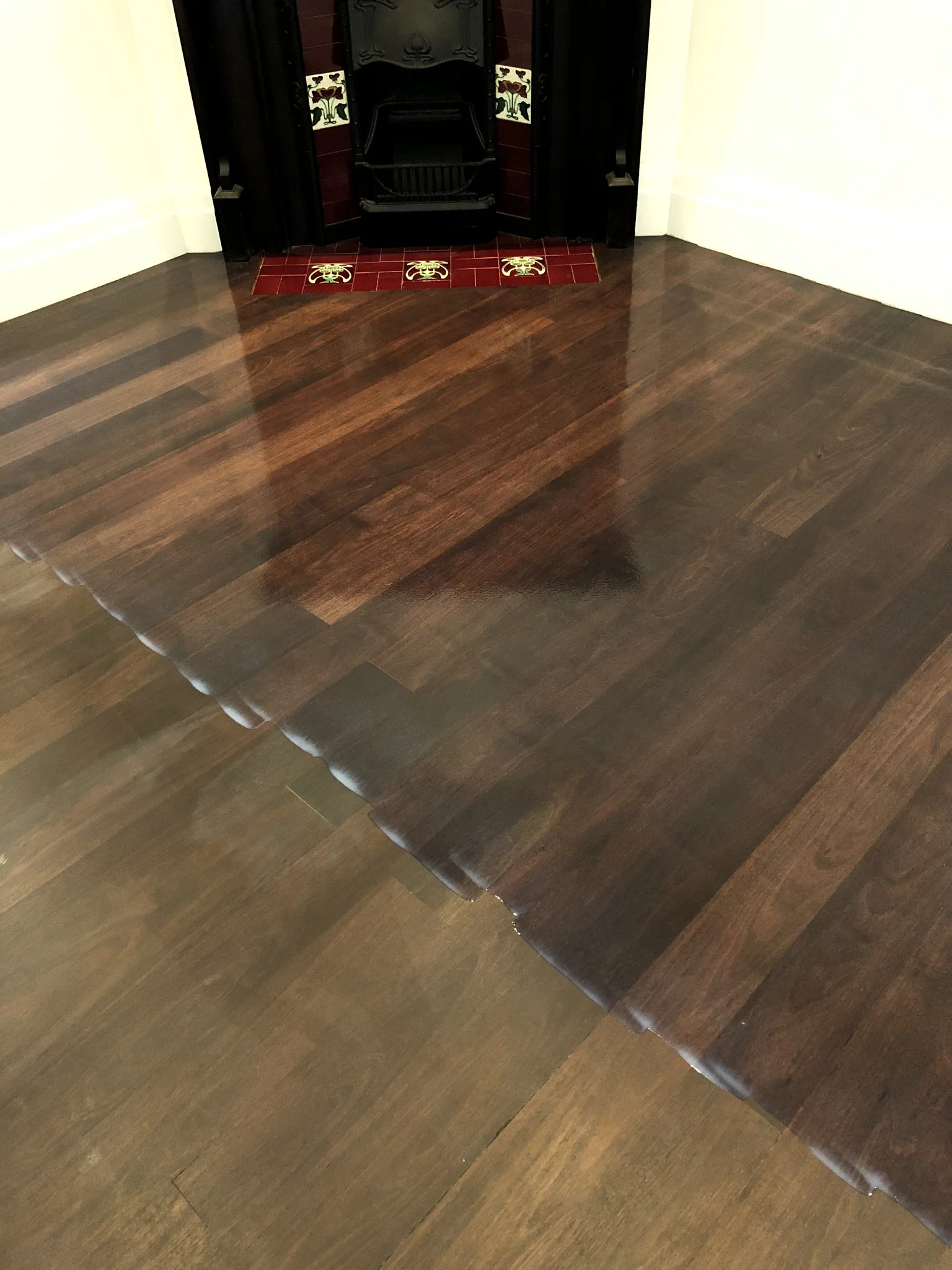 Polished dark wood floor in front of a fireplace with red and black tiles and decorative crab tiles.
