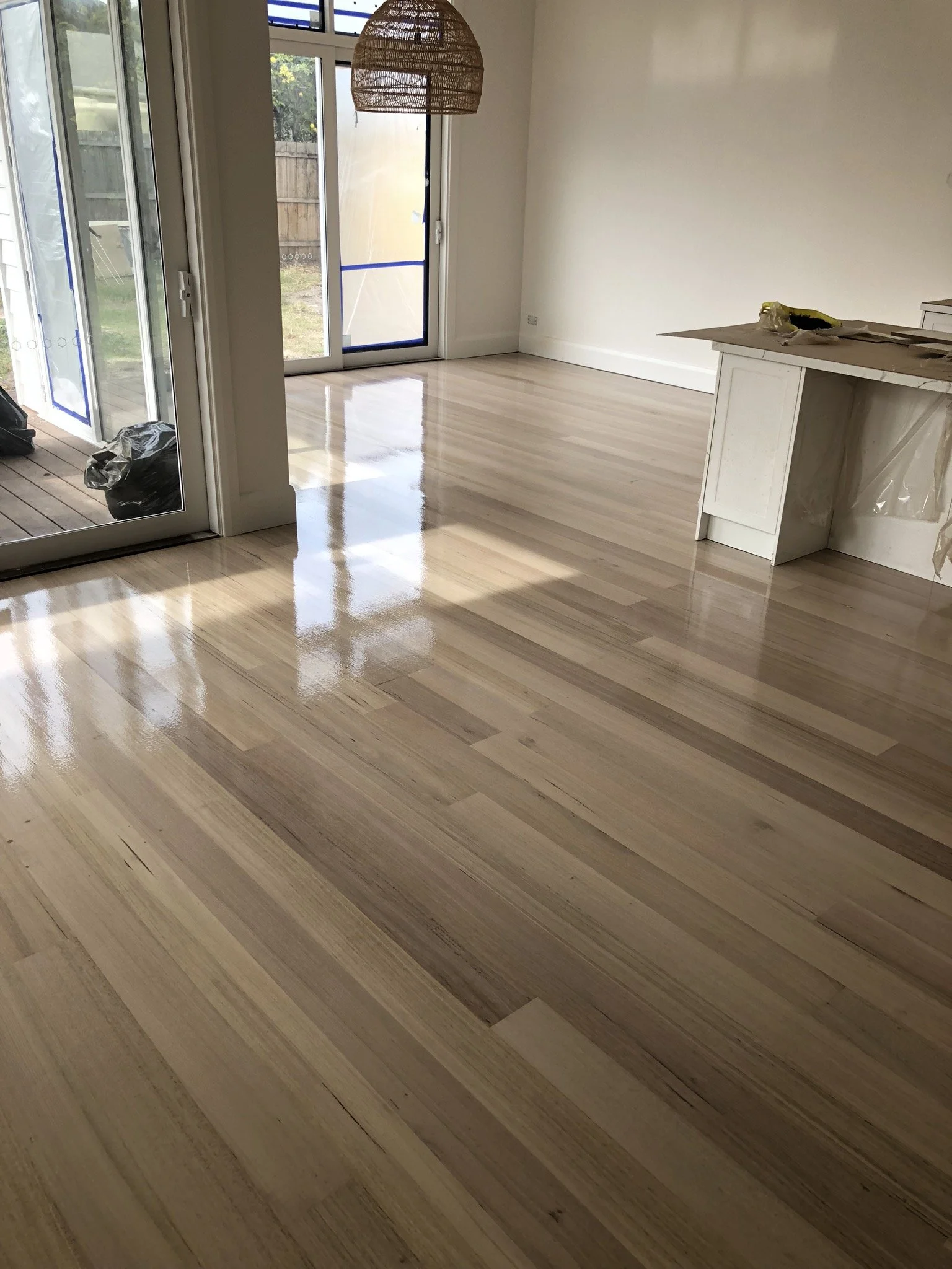 Refinished hardwood flooring in a bright, empty room with large glass sliding doors leading to an outside area.